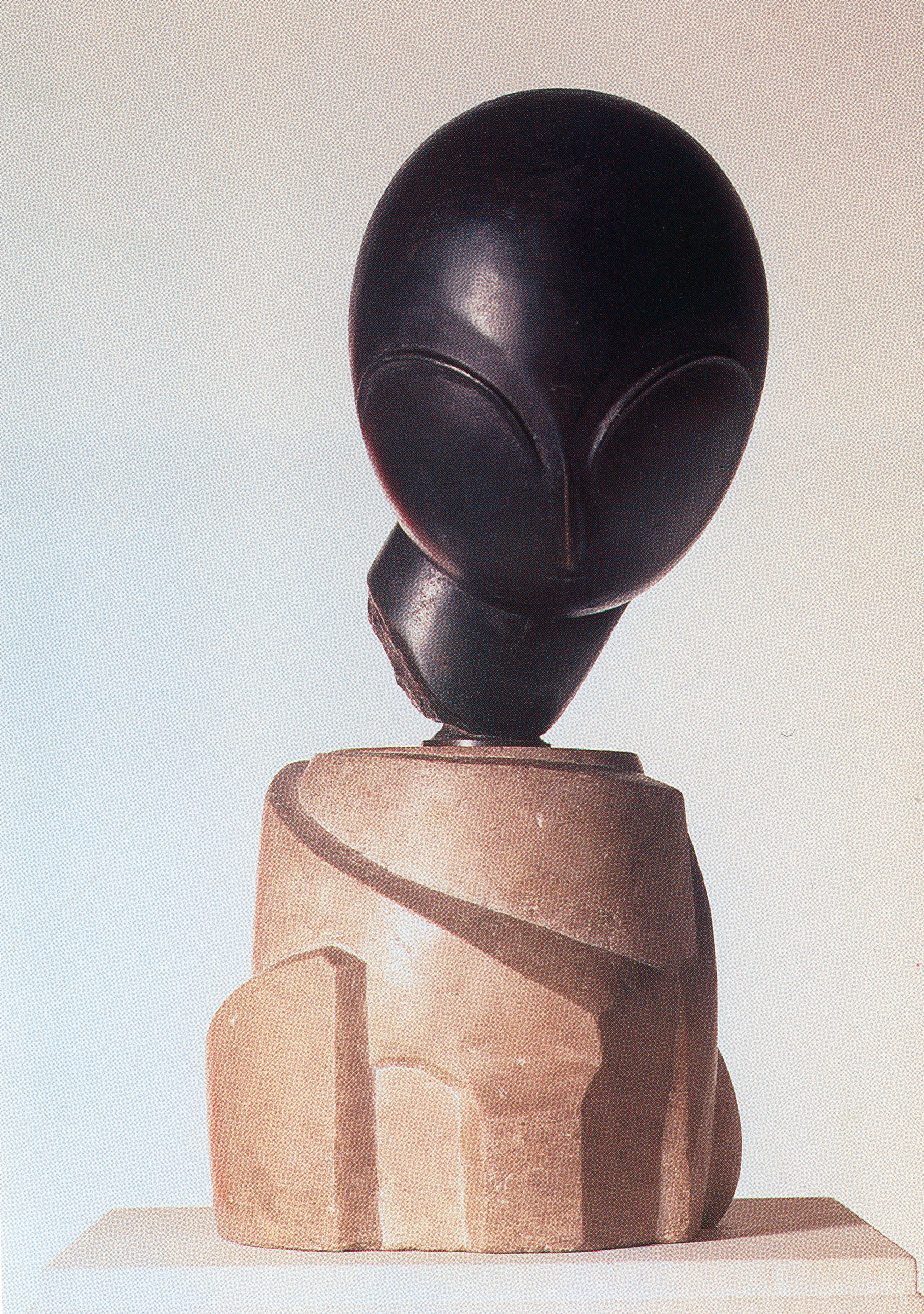 A modern abstract sculpture with a smooth, dark head atop a textured, light-colored base.