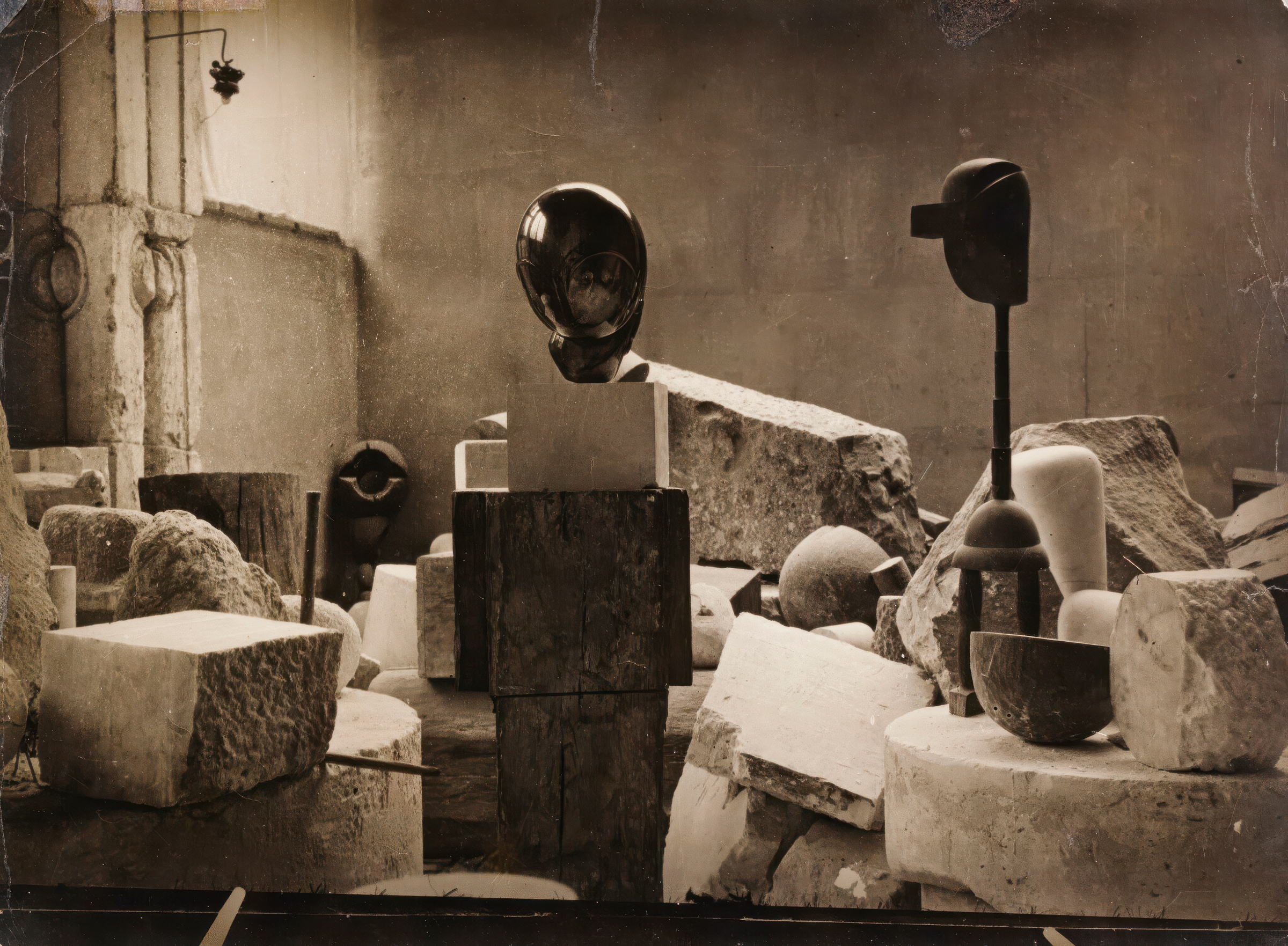 Abstract sculptures and stone blocks are arranged in an artist's studio with rough walls.