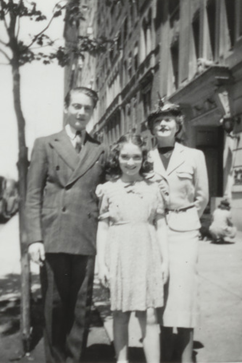 A man, a woman, and a girl pose together on a city sidewalk in a vintage black-and-white photo.