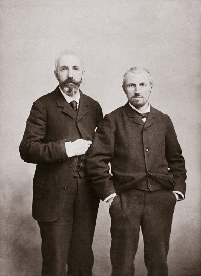 Two men in old-fashioned suits pose together in a vintage black-and-white photograph.