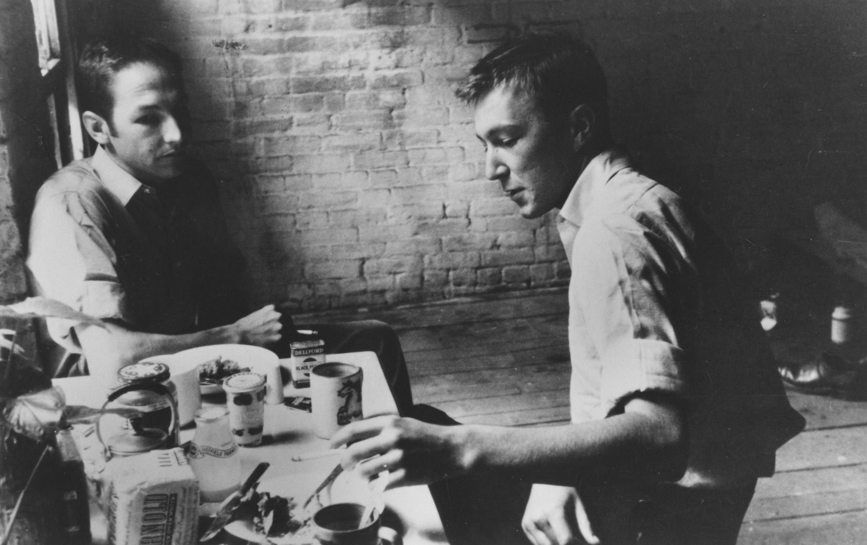 Two people sit at a small table with food and drinks in a dimly lit room with brick walls.