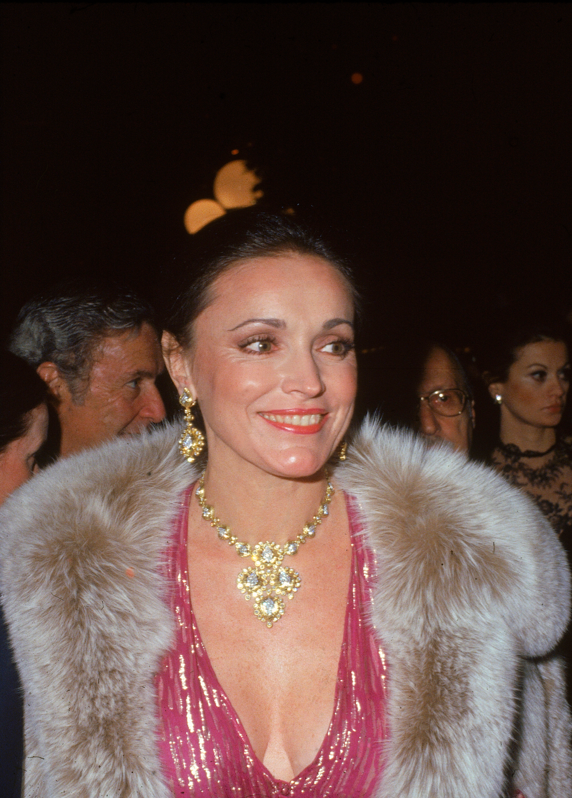 A woman in a pink dress with a fur shawl and elaborate jewelry at a formal event.