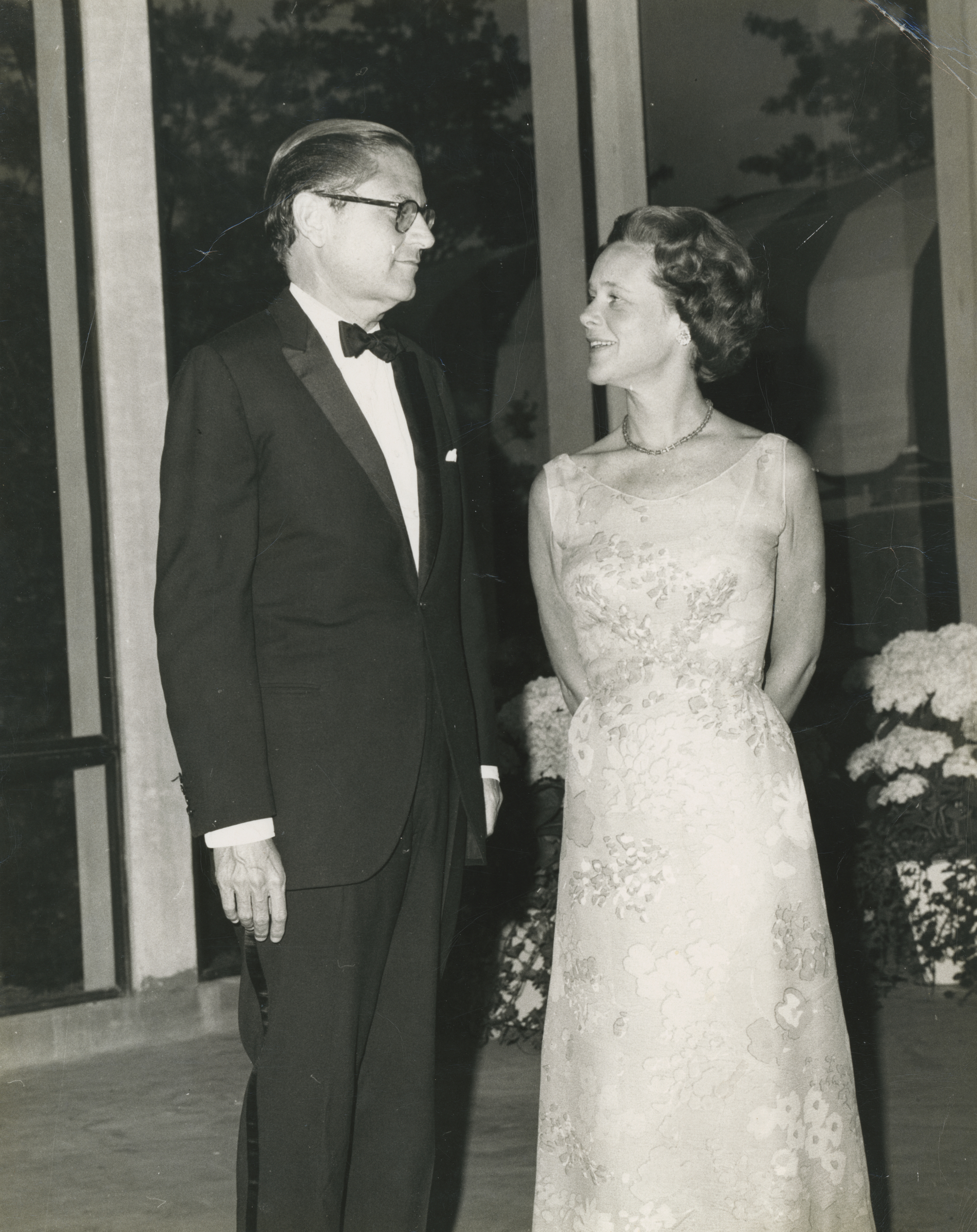 A man in a tuxedo and a woman in a floral gown stand together at a formal event.