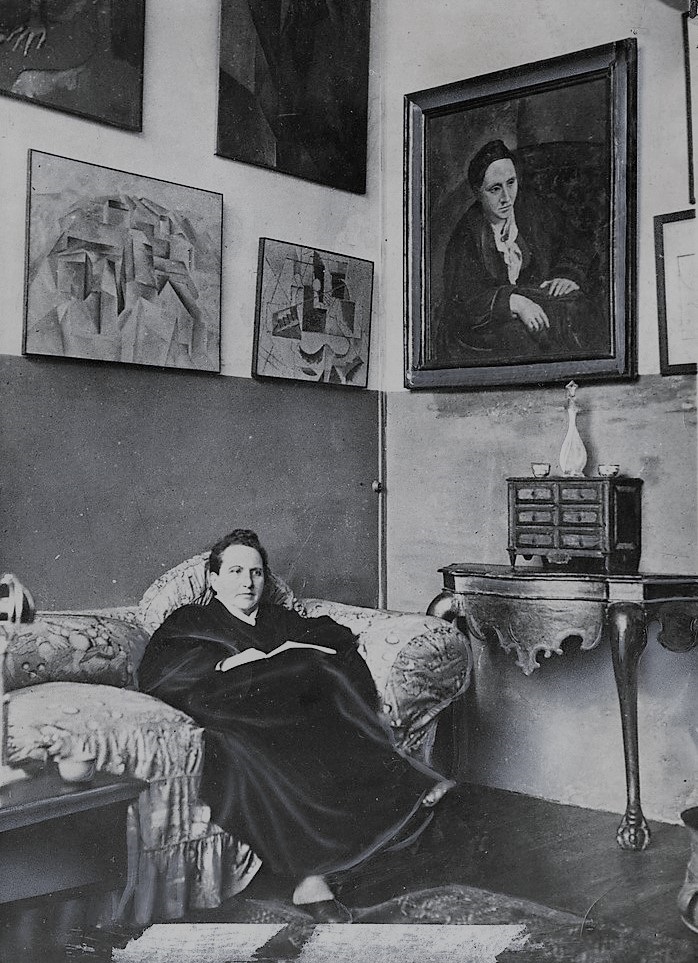A person sits on a sofa in an art-filled room with paintings and a decorative table.