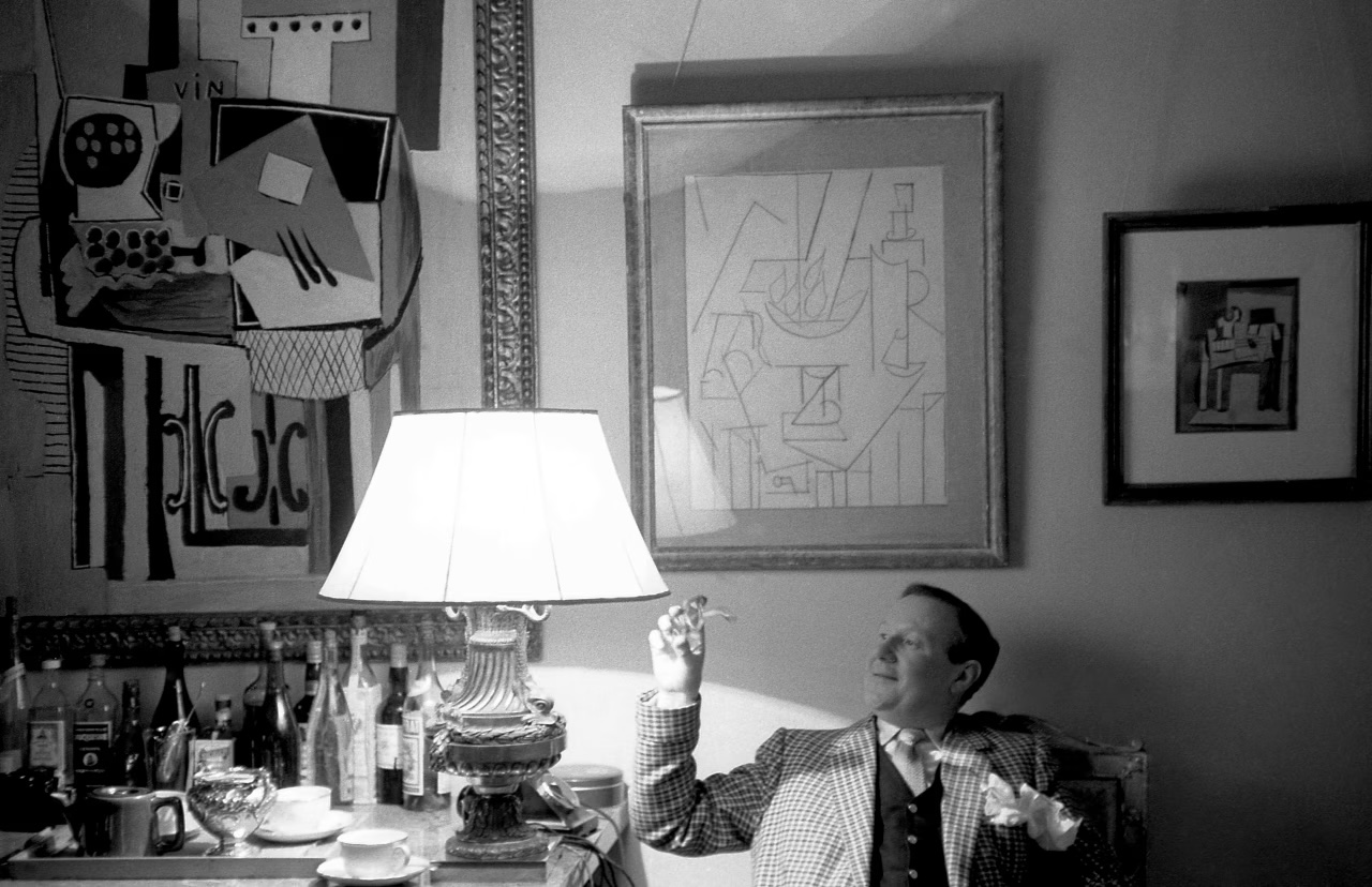 A person sits at a table with drinks, under a lamp, surrounded by abstract artwork on the wall.