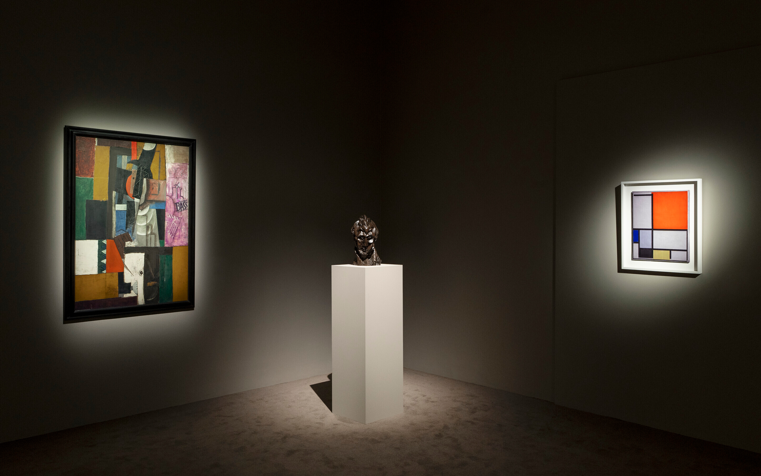 A dimly lit art gallery displays two abstract paintings and a sculpture on a pedestal.