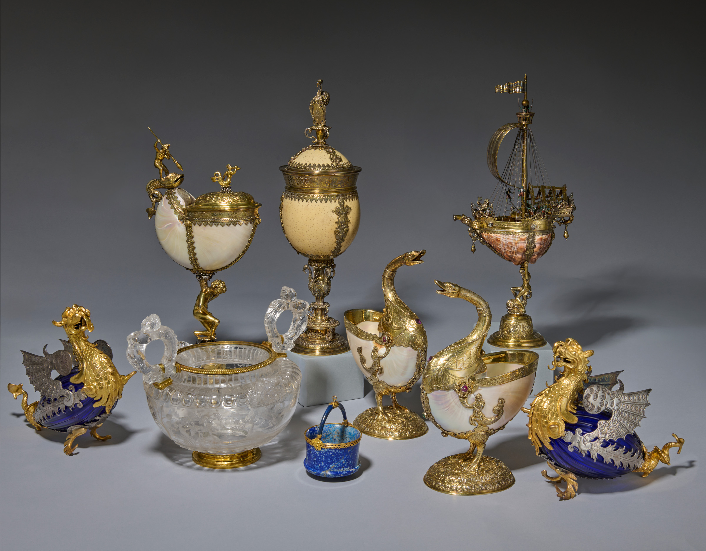 A pair of silver- and gilt-copper-mounted blue glass dragons, Italian, probably Florence, circa 1615, one on either side of the group. The other objects, clockwise from left: a Continental parcel-gilt silver-mounted nautilus shell cup, Central Europe, circa 1640; a German parcel-gilt silver-mounted shell nef, Bremen, circa 1600; a pair of German jewelled silver-gilt-mounted nautilus cups, circa 1602; a fine small gold-mounted lapis lazuli bucket, Florence or Milan, last quarter of the 16th century; a rock crystal vase, Milan, circa 1550-75, the handles and mounts later. All offered in The Exceptional Sale: Masterworks Across Cultures on 30 June 2026 at Christie's in London