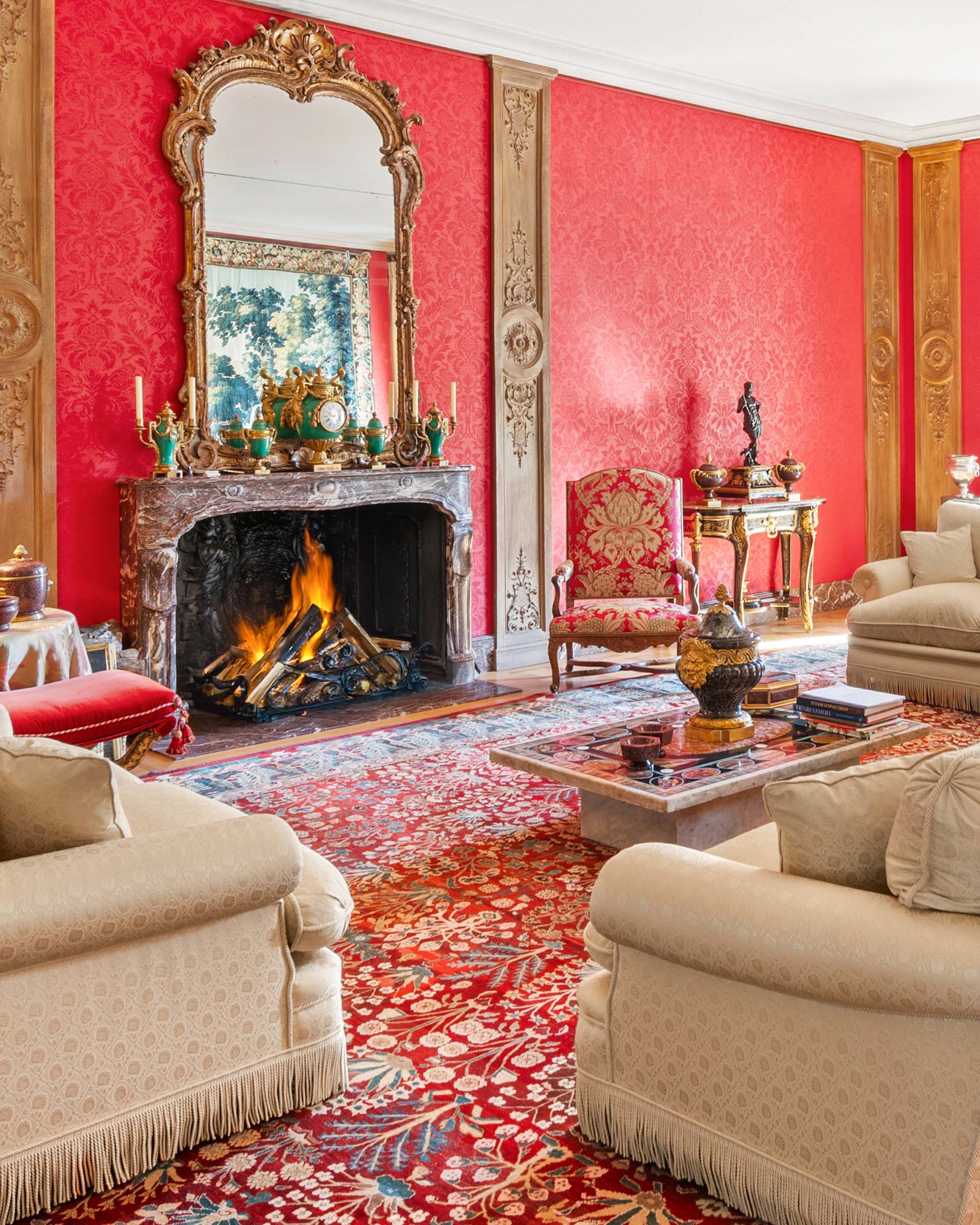 The grand salon of the Chateau de Tournay, with its marble fireplace and walls covered in crimson damask