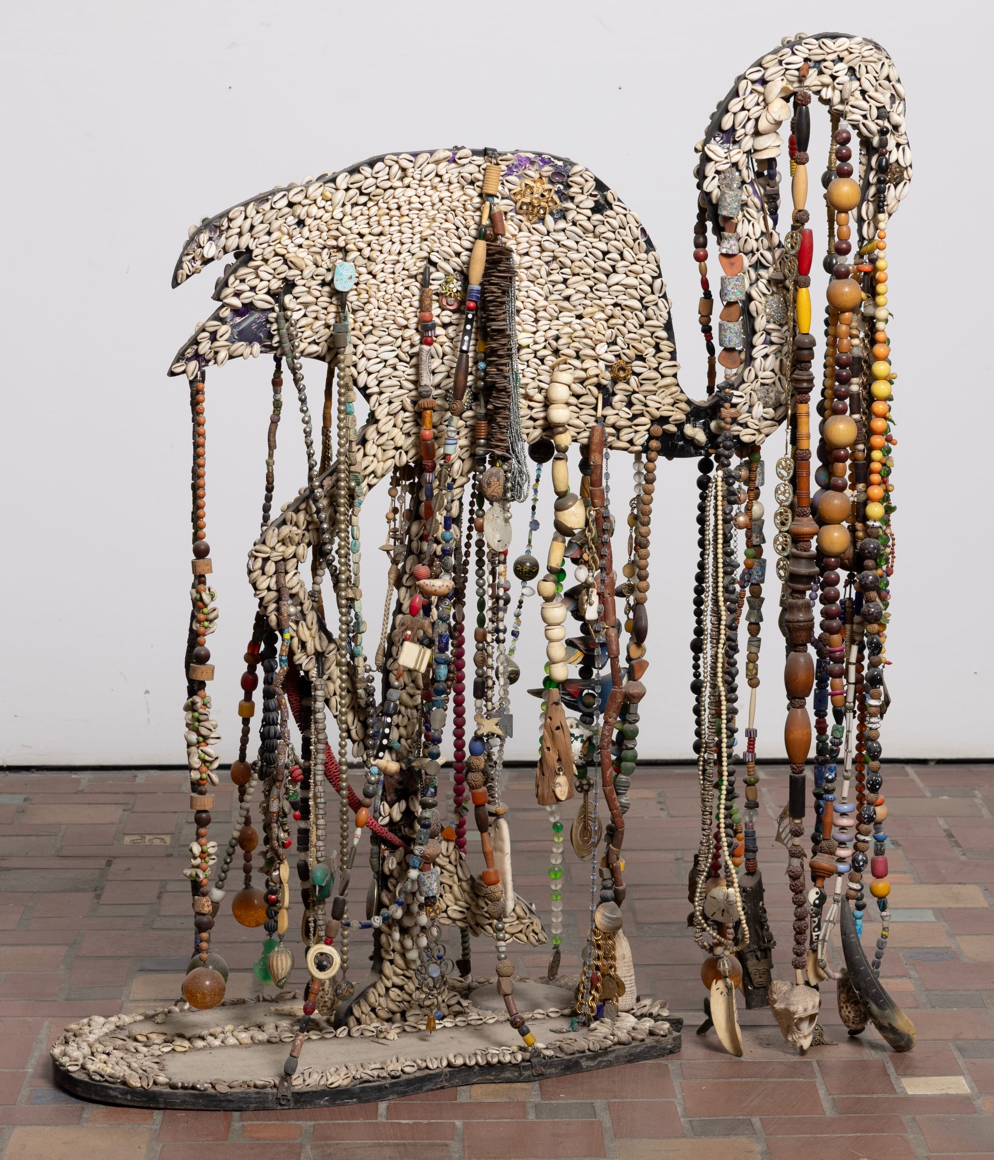 A beaded and shell-covered sculpture shaped like a bird with strings of colorful beads hanging down.