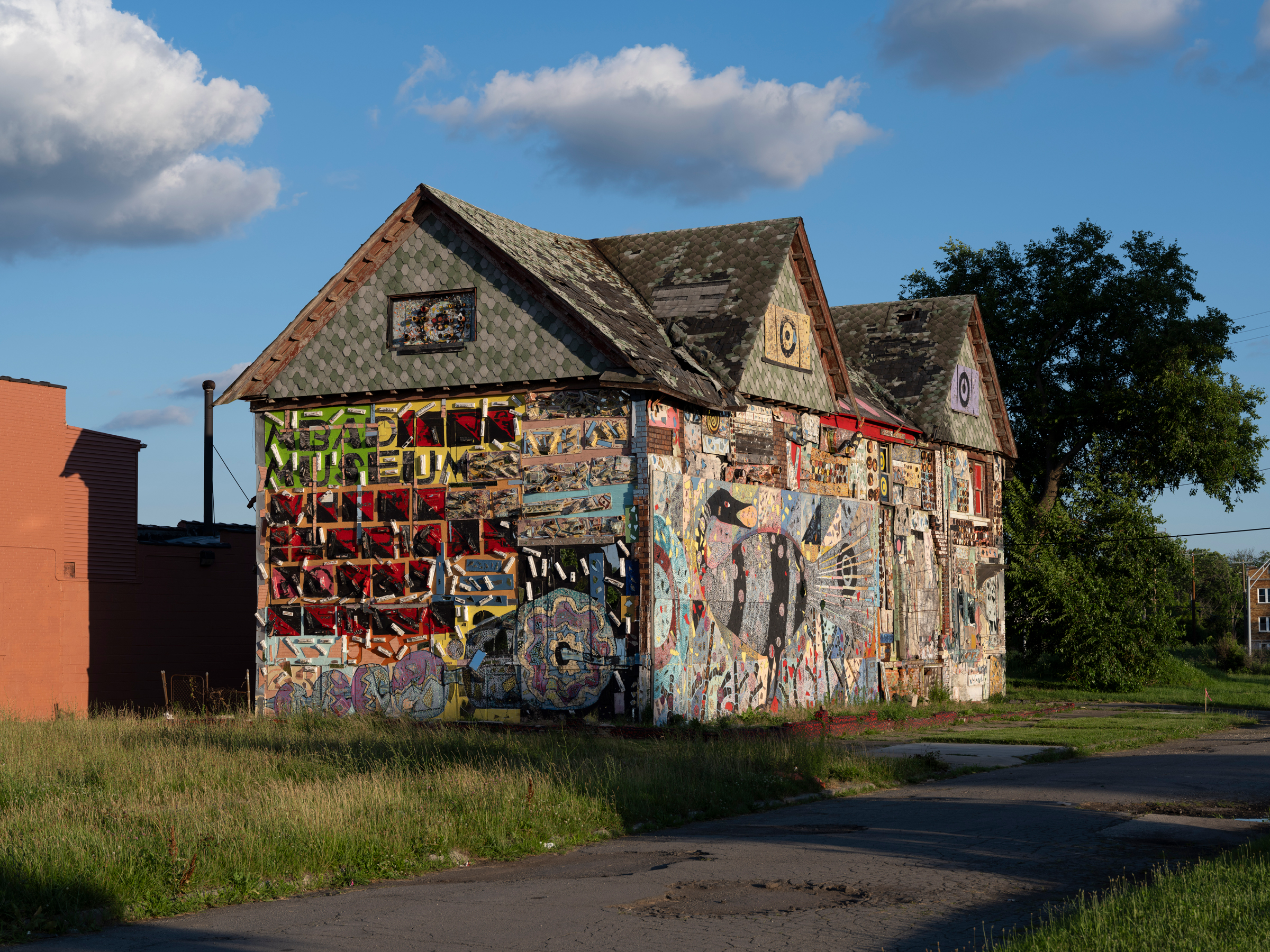 A deteriorating house covered in colorful graffiti and murals stands in a grassy area.