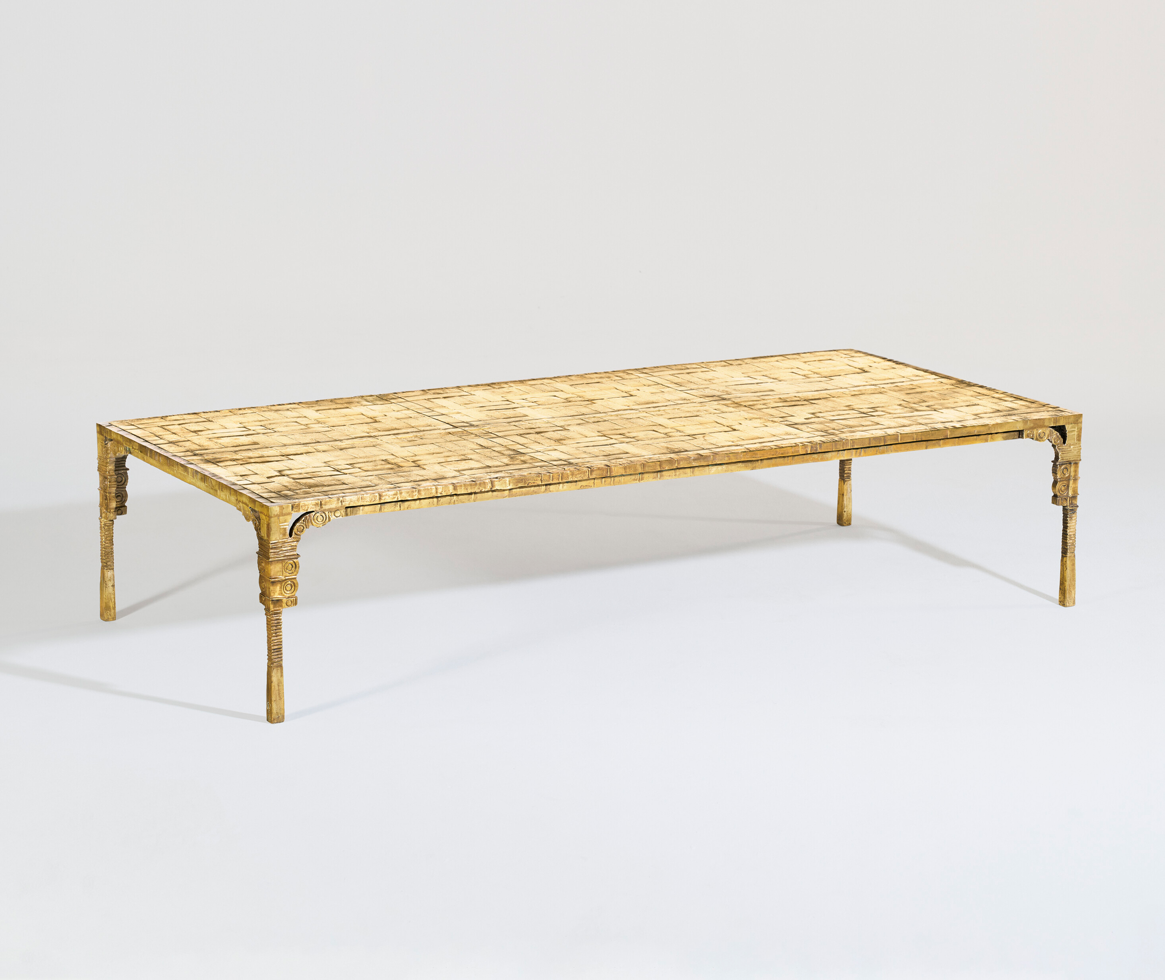 A low, rectangular table with a yellowish, textured surface and intricately designed legs.