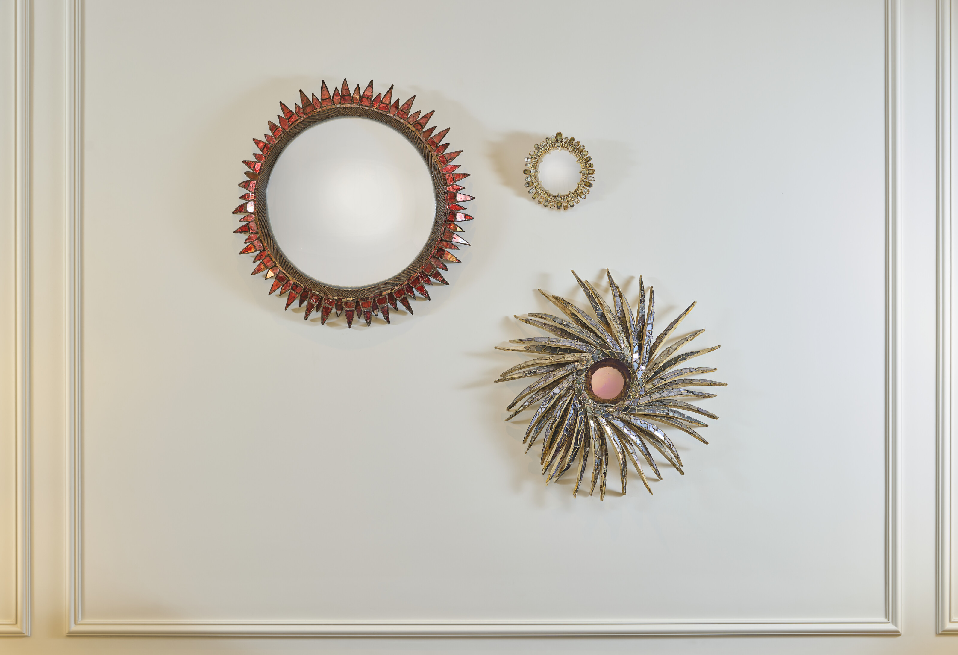 Three decorative circular mirrors with unique frames are mounted on a white wall.