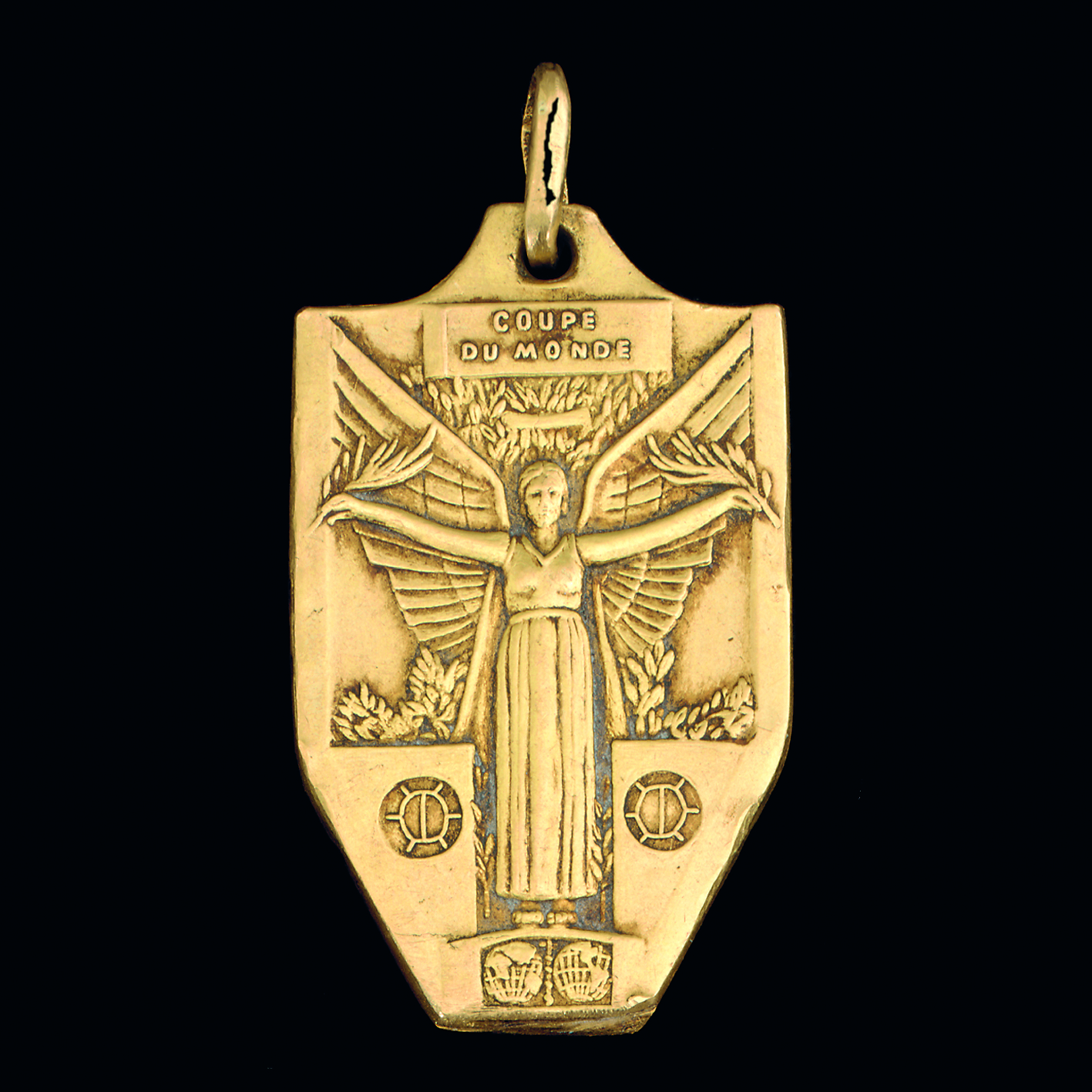A gold medal with an engraved winged figure and the text "Coupe du Monde" at the top.