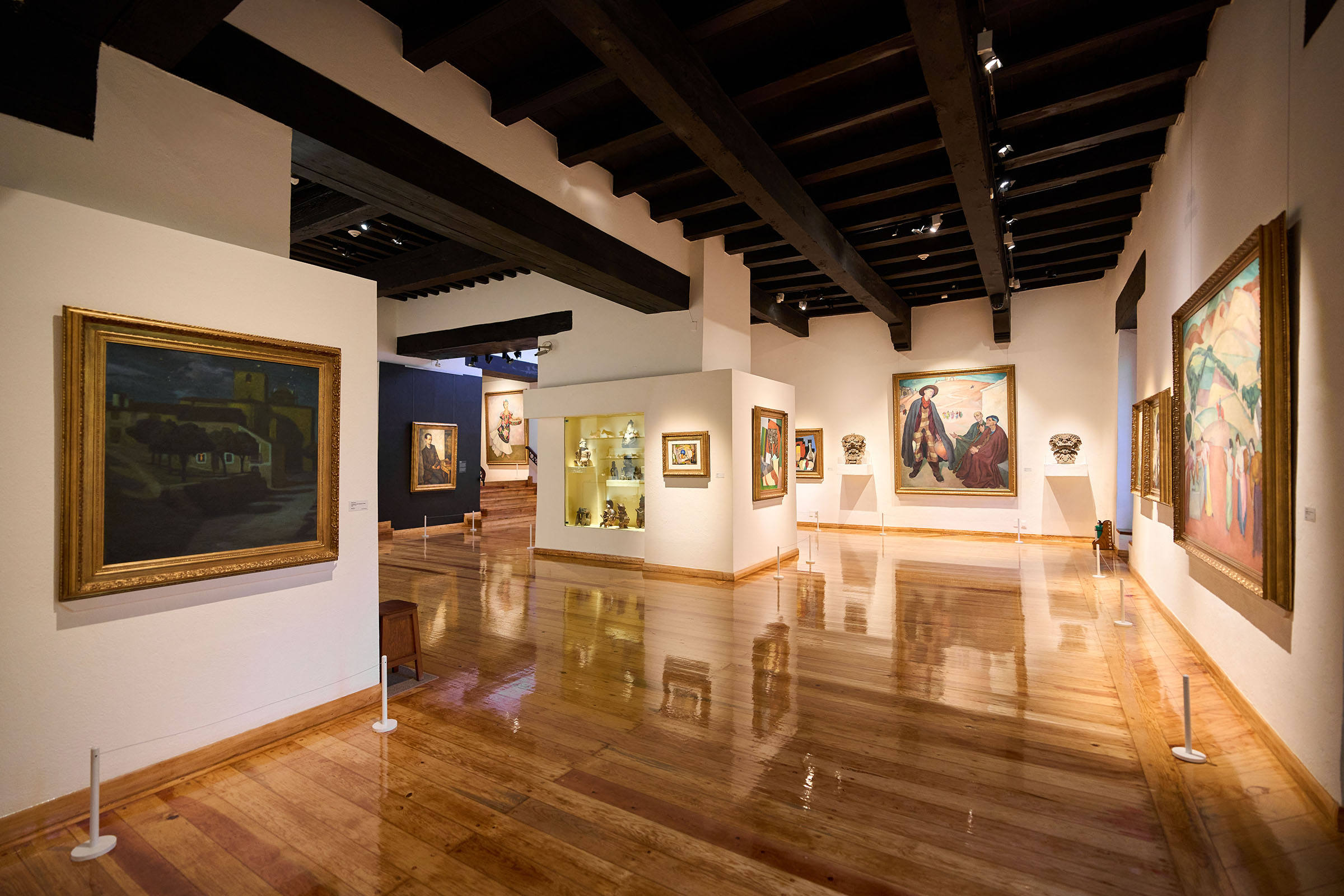 A gallery space at the Dolores Olmedo Museum, featuring works by Diego Rivera and a selection of pre-Columbian artefacts. On the wall to the left is Rivera’s 1907 work Night Scene in Avila; on the wall at the very end is his The Outskirts of Toledo from 1912