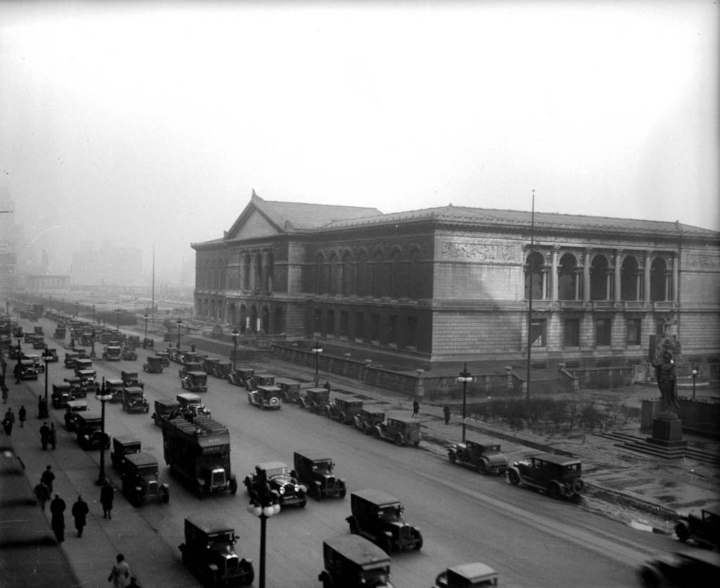 A historic city street scene with vintage cars and a large classical-style building.