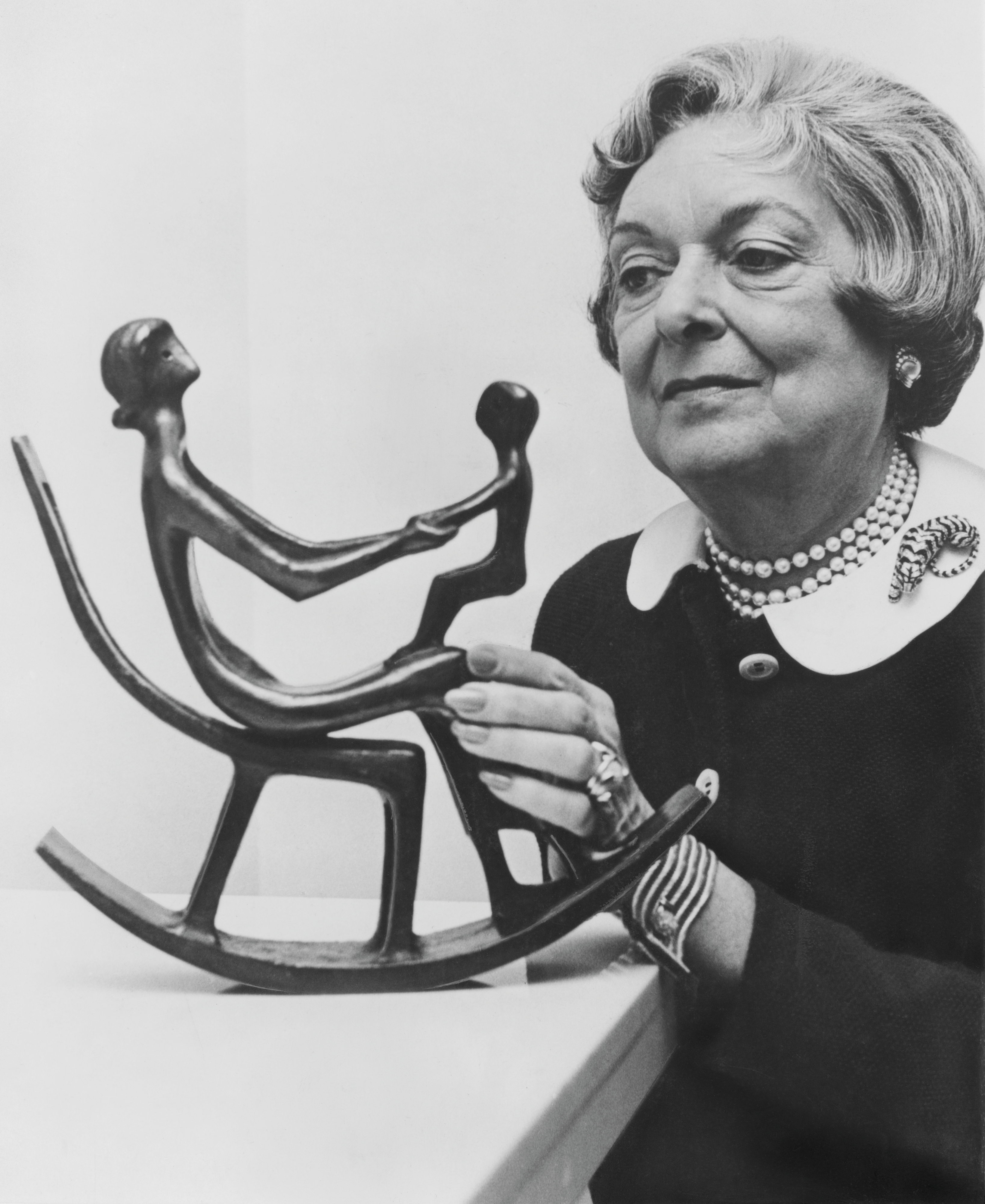 A woman holds a modern sculpture of two abstract figures on a rocking base.