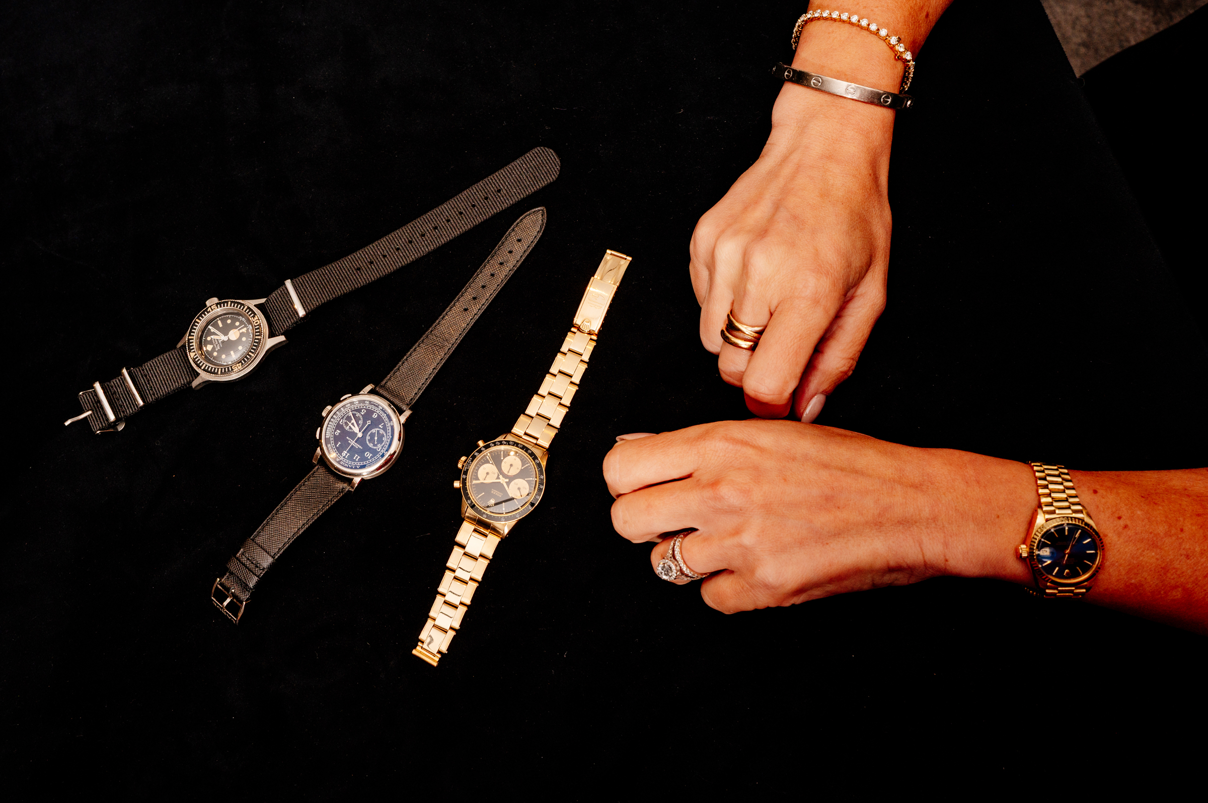 Two hands wearing jewelry are displayed next to four wristwatches on a black surface.