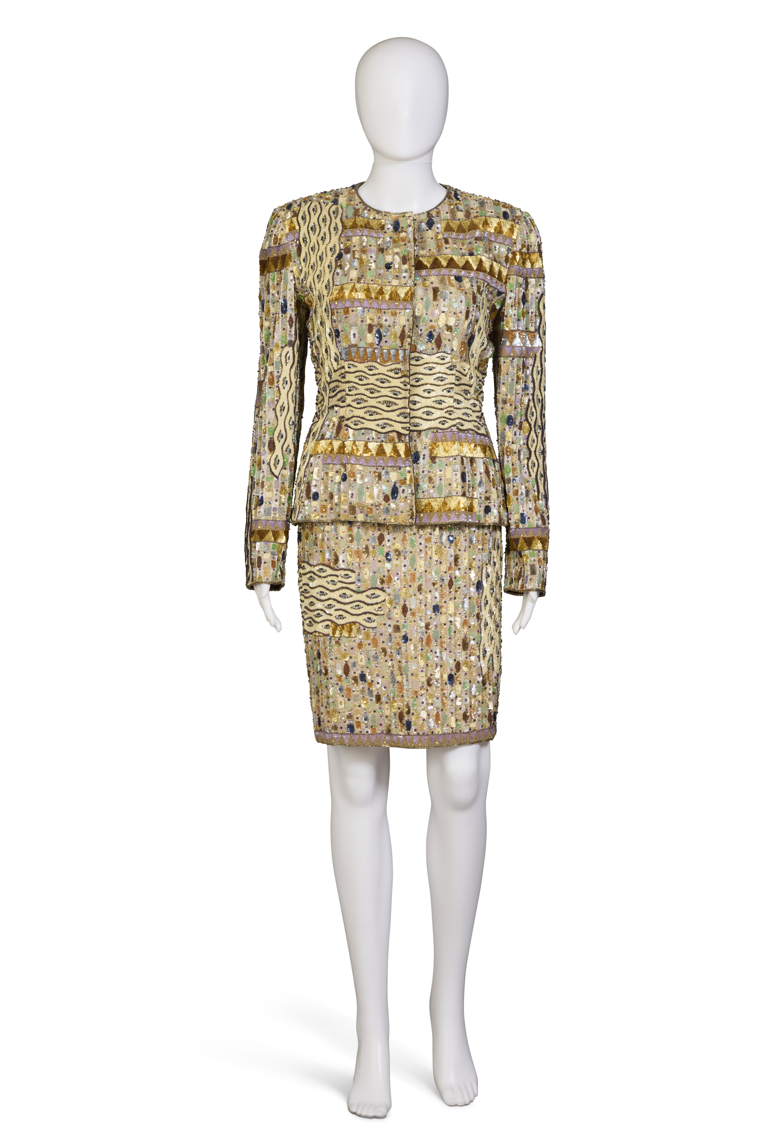 A mannequin wears a patterned, gold-toned skirt suit with intricate embellishments.