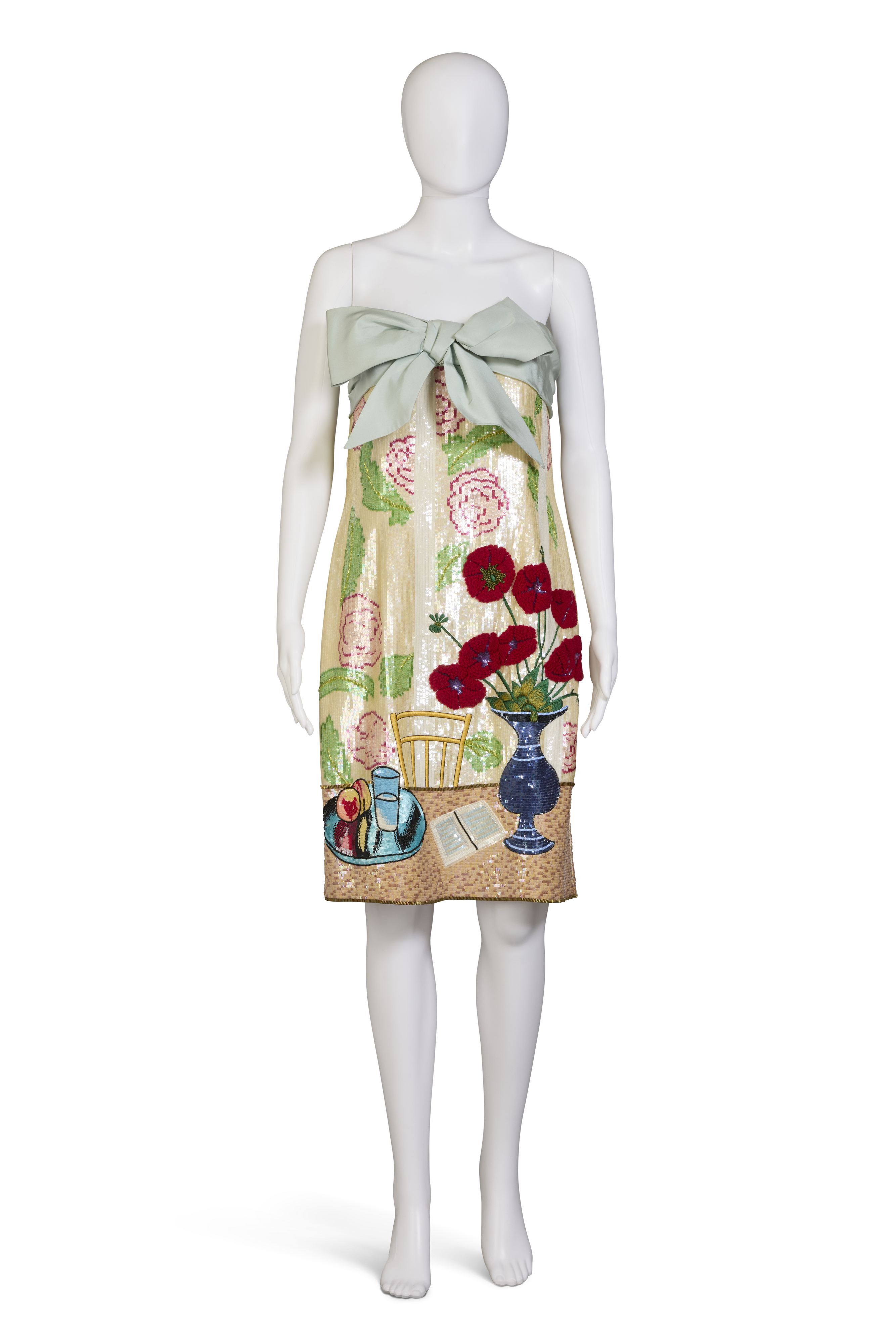 A mannequin wears a strapless dress with a large bow and a colorful still-life scene print.