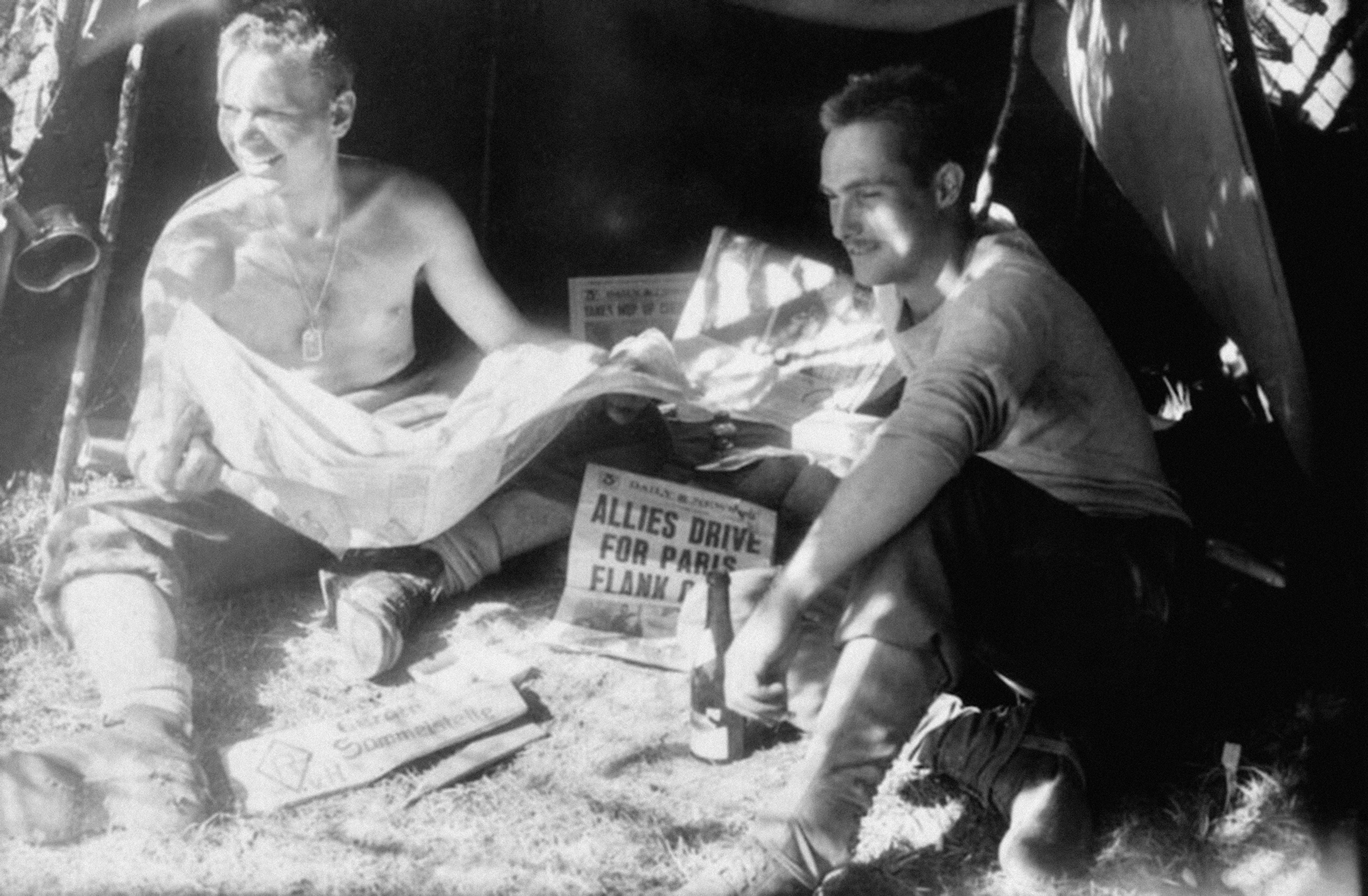 Two soldiers relax in a tent while reading newspapers during wartime.