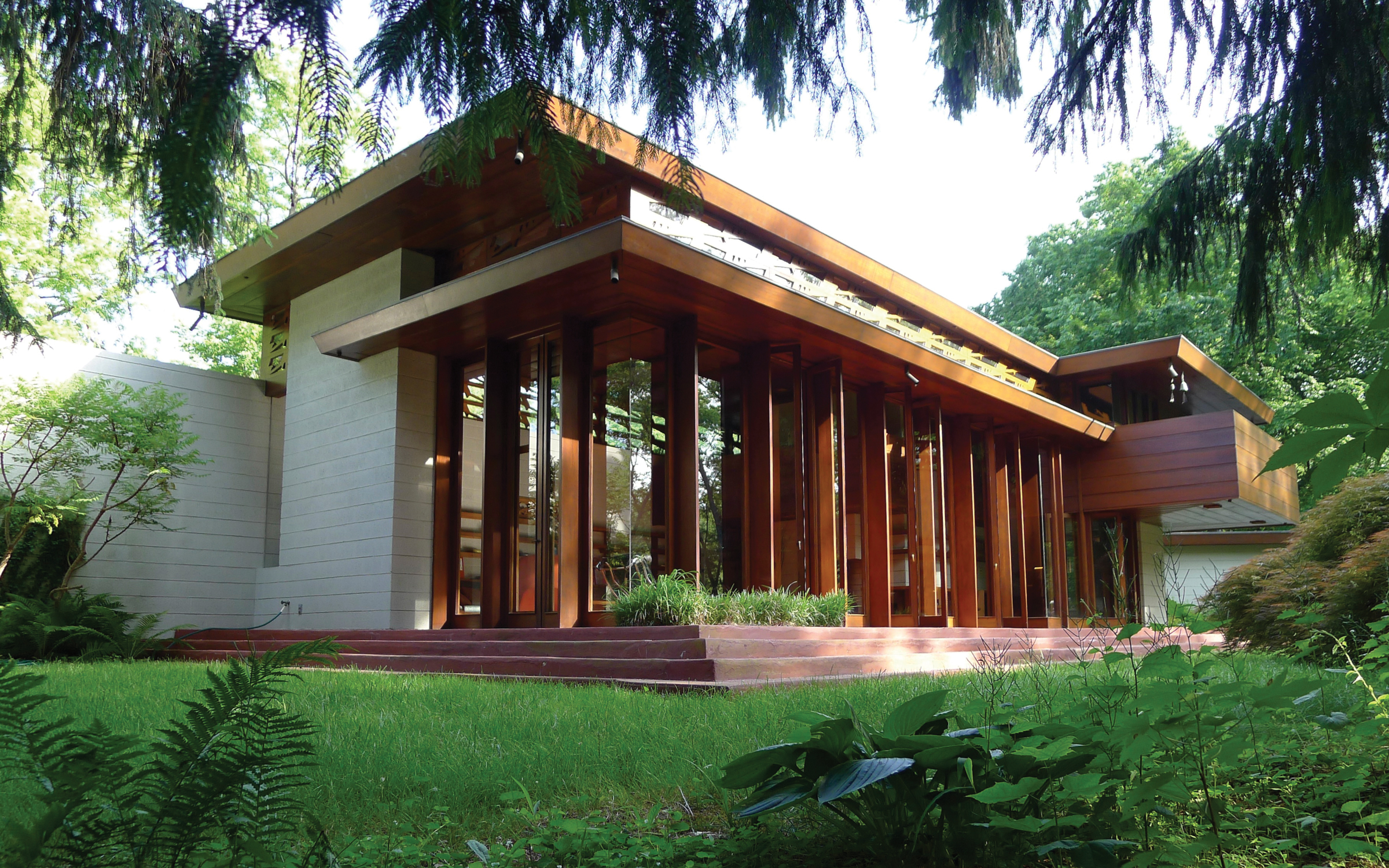 A modern house with large vertical windows and a flat roof in a lush green garden setting.