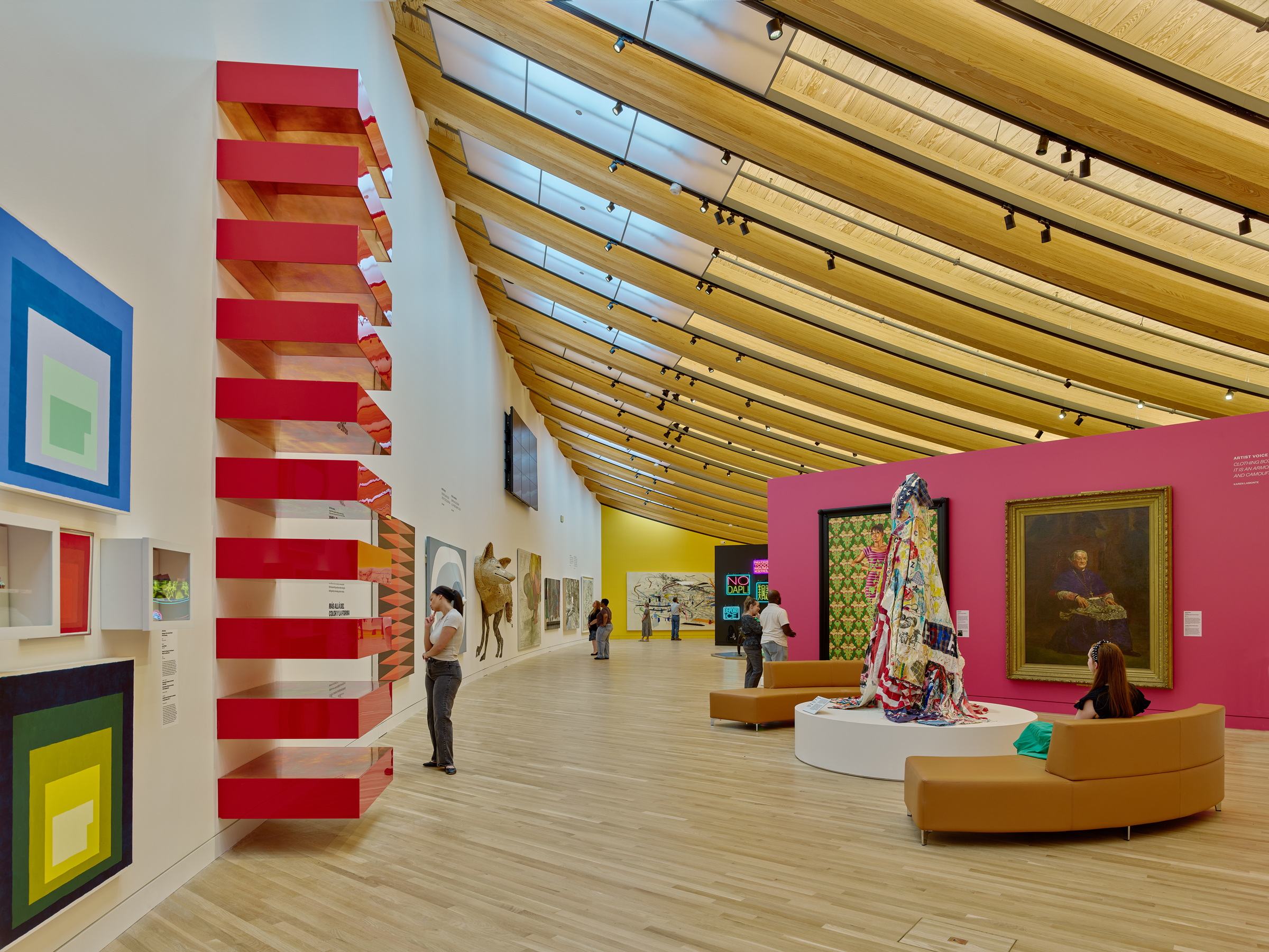 A modern art gallery features colorful abstract pieces, sculptures, and visitors observing the displays.