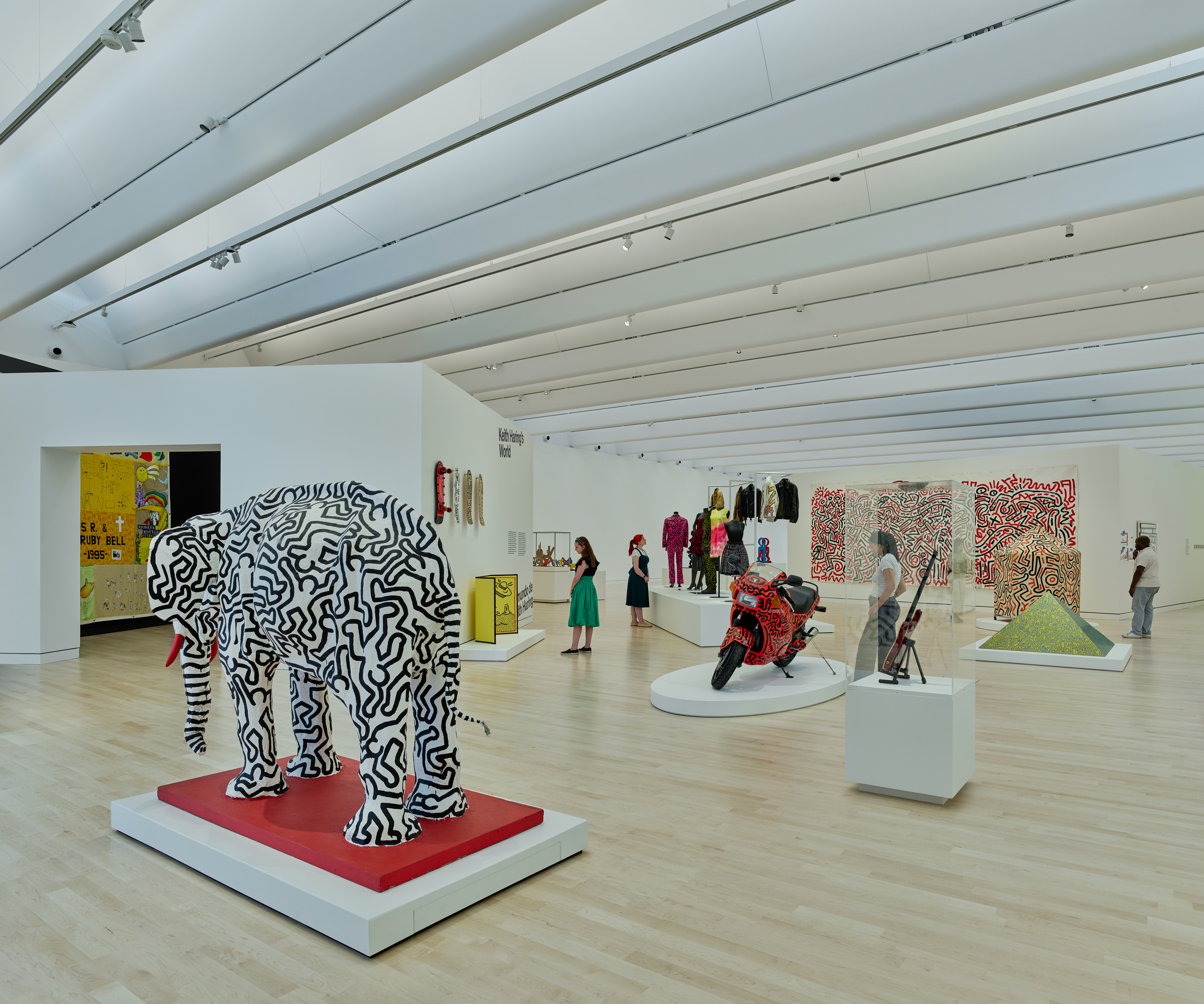 A modern art gallery features colorful sculptures, a painted elephant, and visitors observing exhibits.