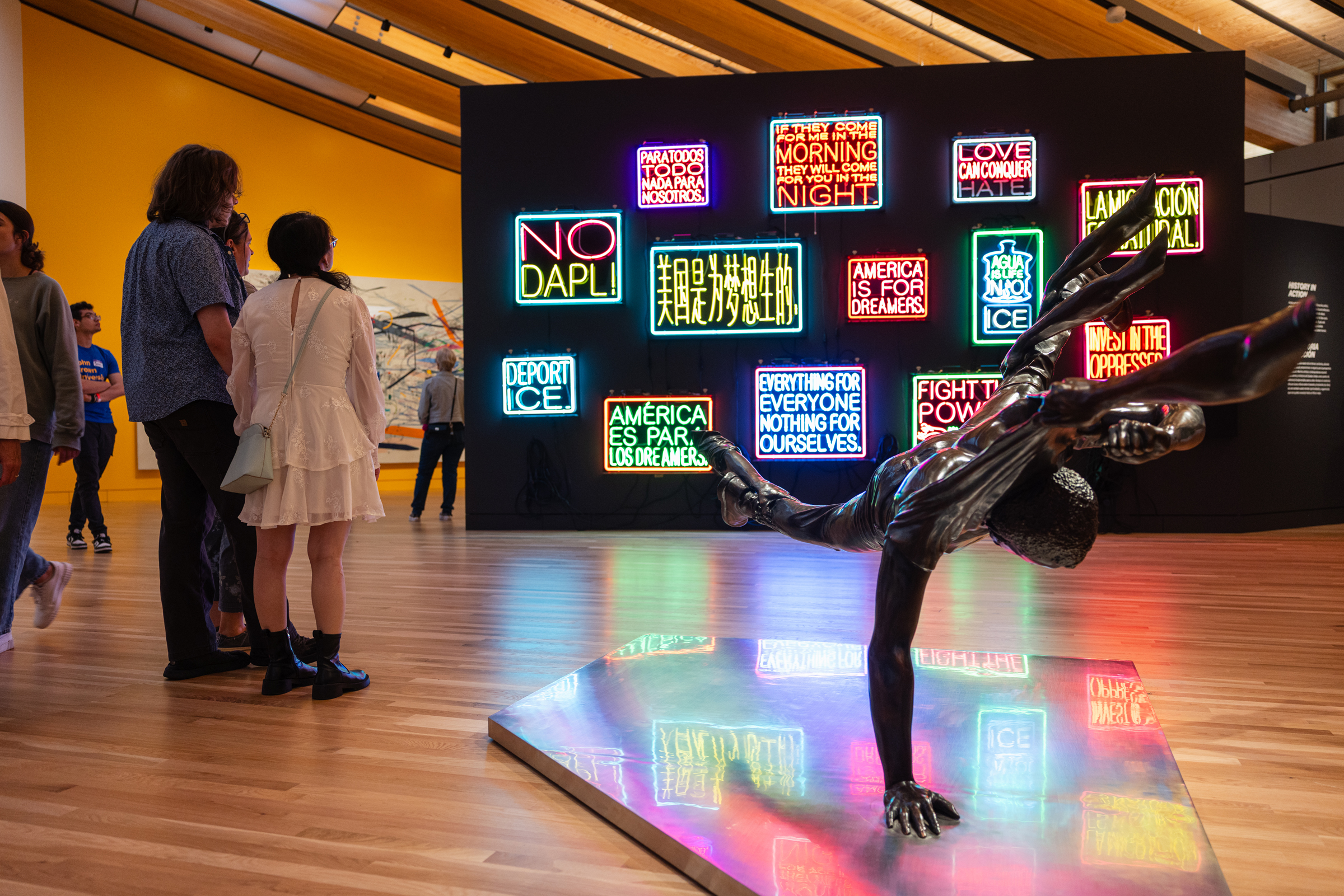 People view colorful neon signs and a dynamic sculpture in a contemporary art gallery.