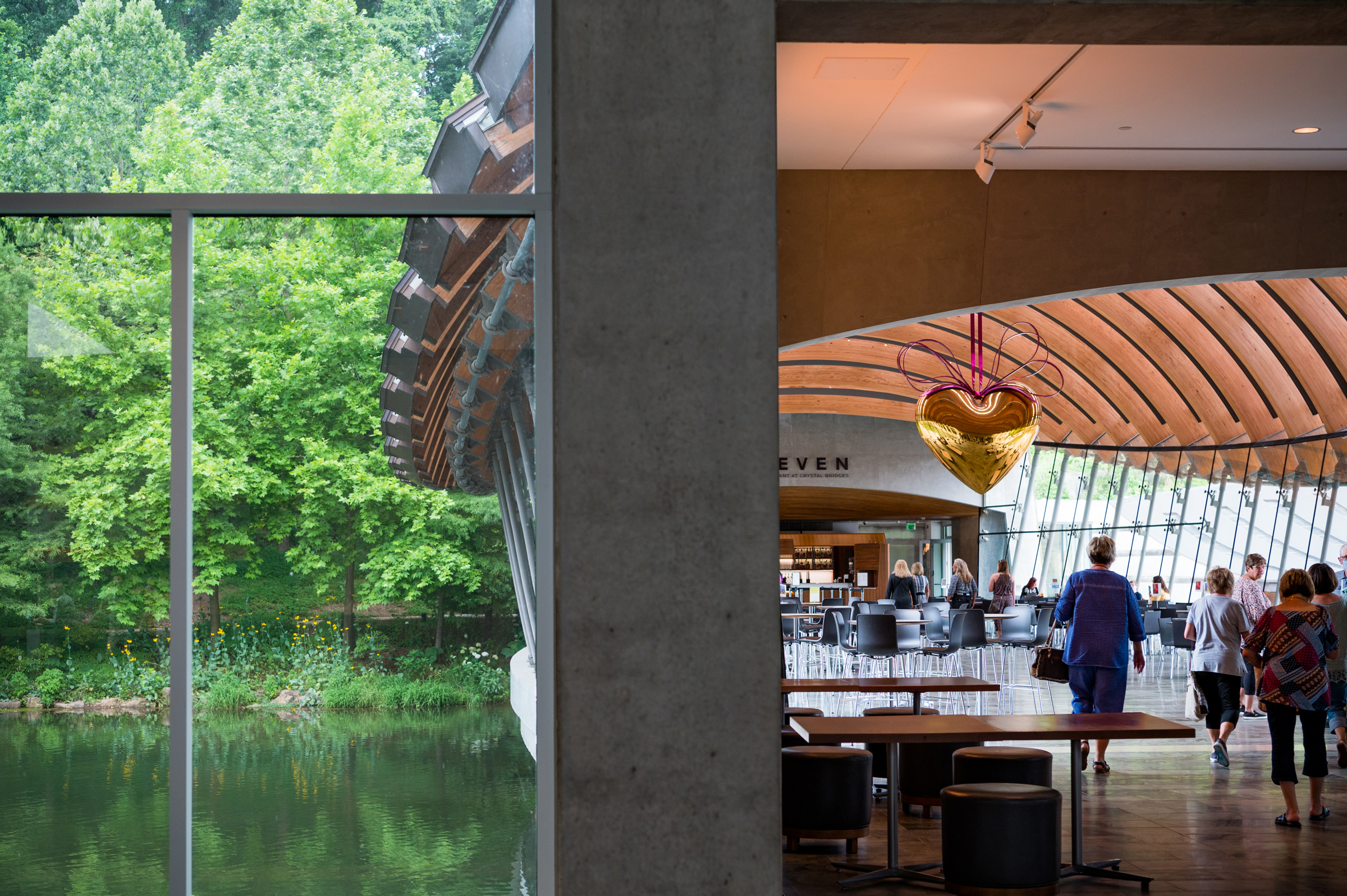 A modern building interior with large windows overlooks a pond and lush green trees outside.