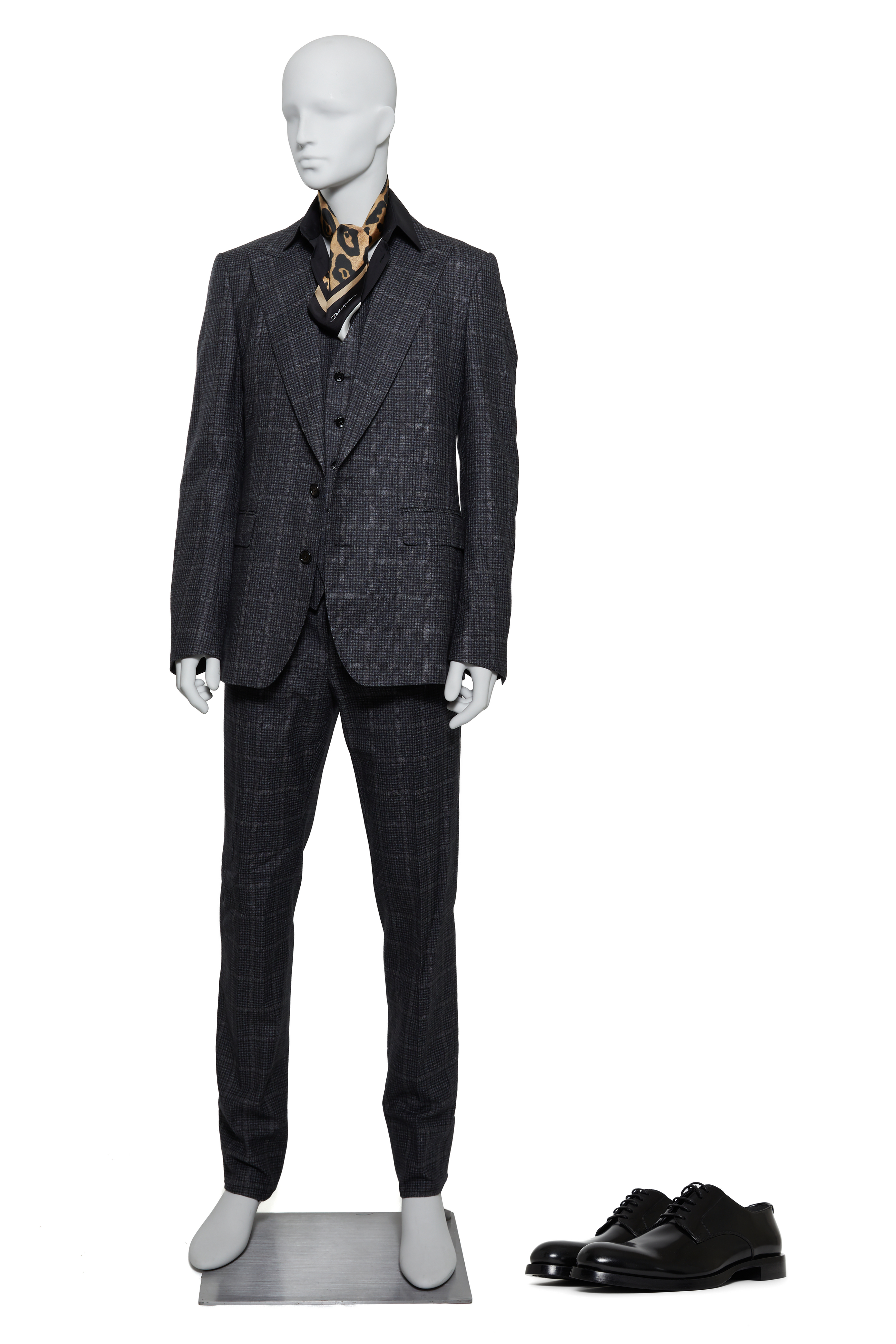 A mannequin in a plaid suit, leopard print scarf, and black shoes placed nearby.