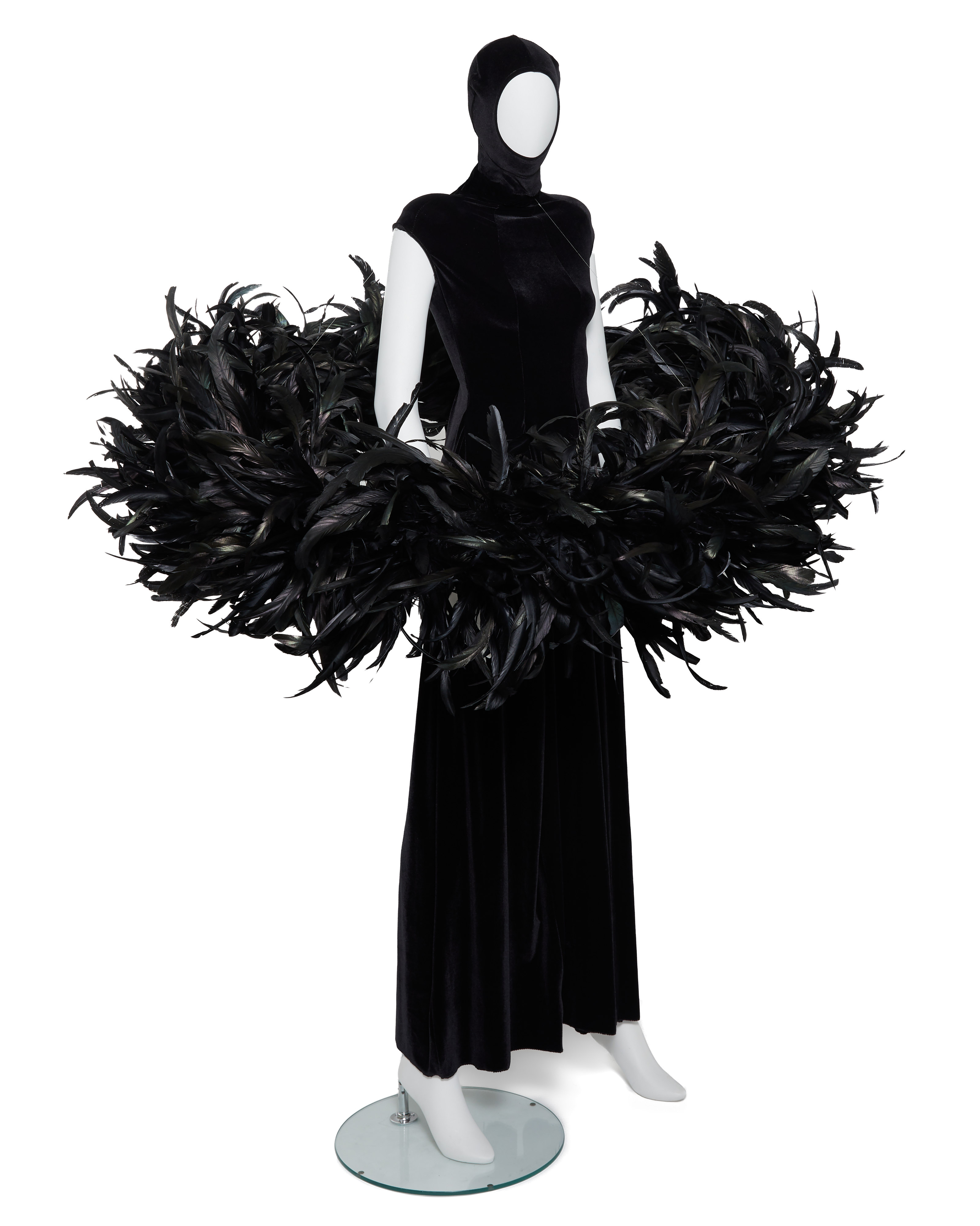 A mannequin wears a black velvet gown with a dramatic, wide collar of black feathers.
