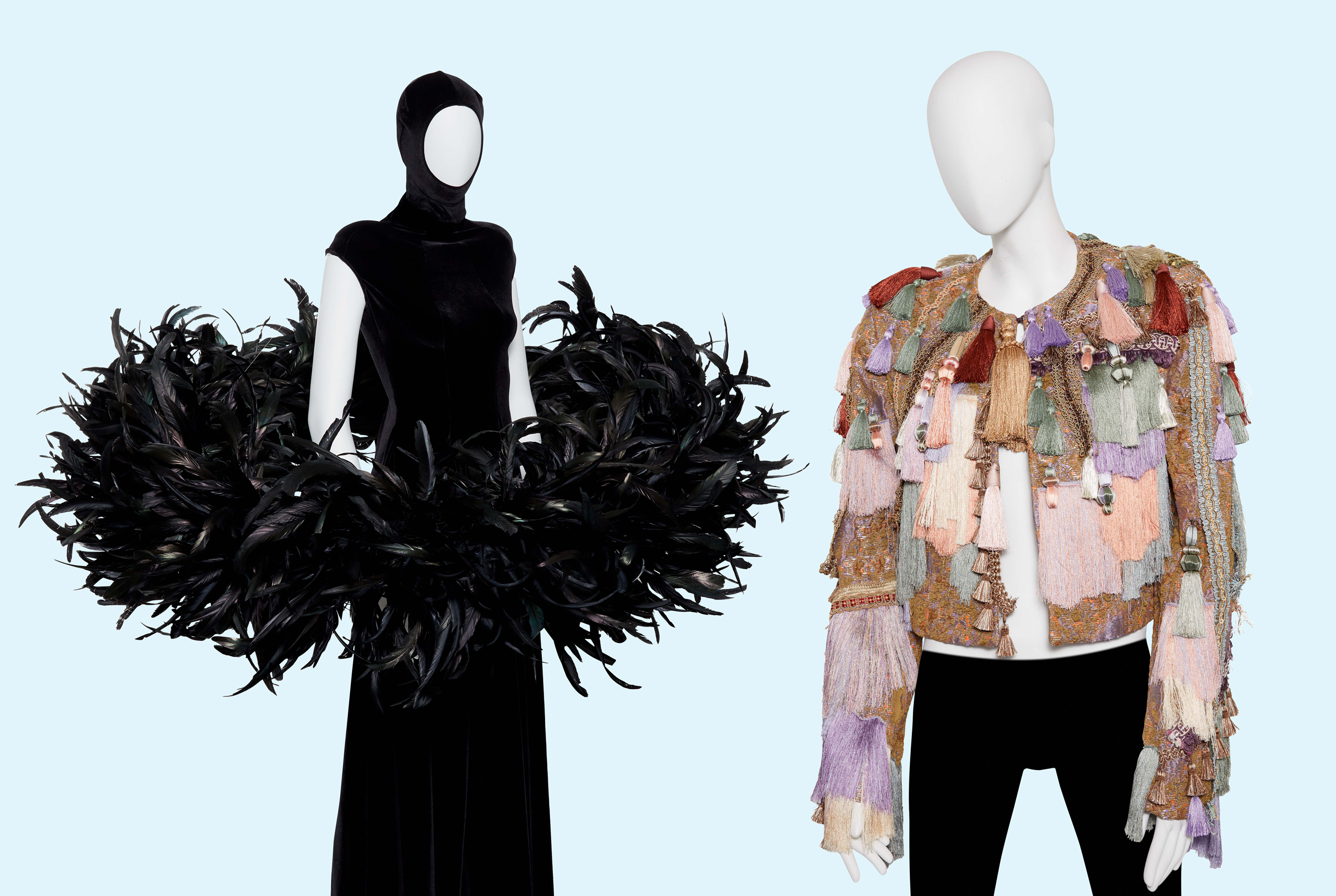 Two mannequins display avant-garde outfits: one with a black feathered ensemble, the other with a colorful tassel jacket.