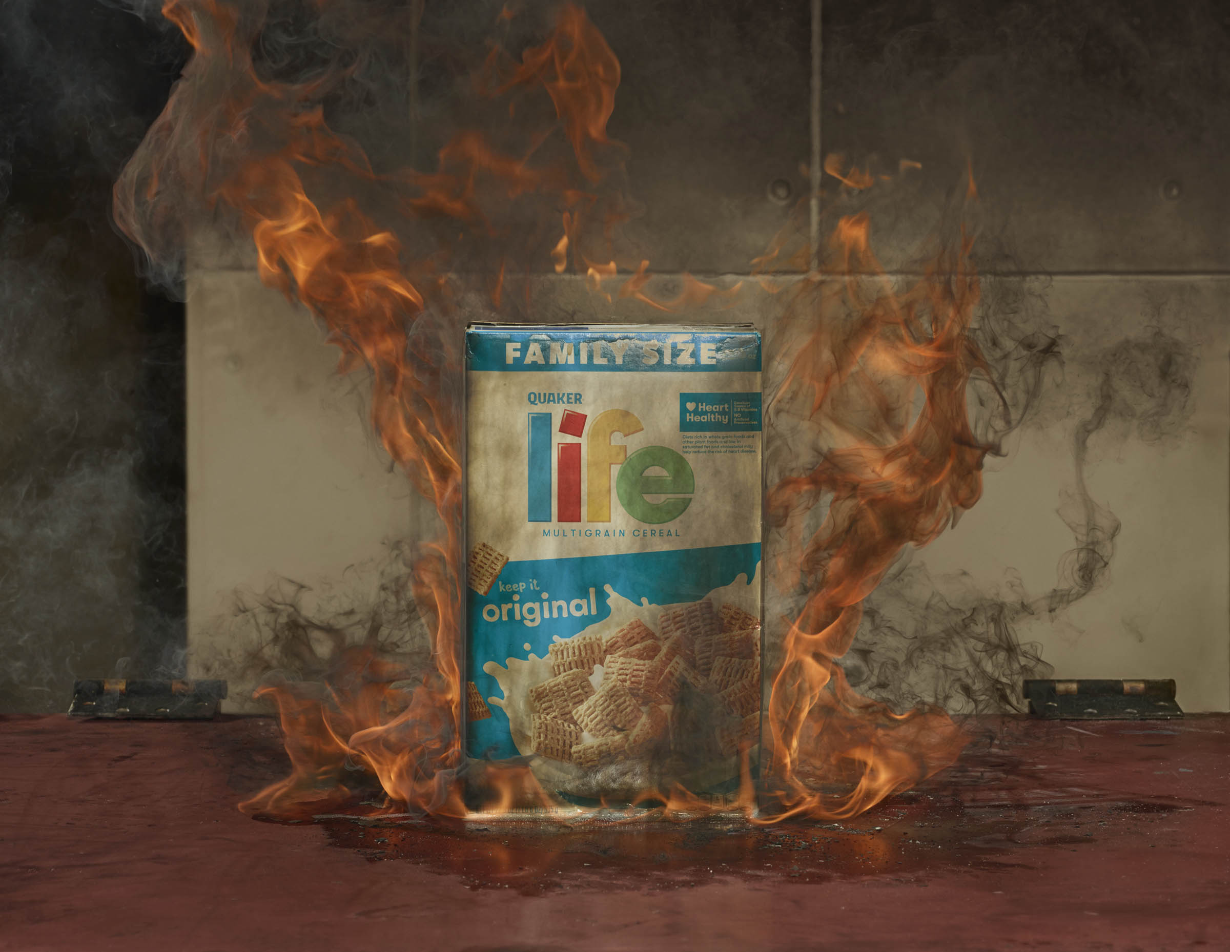 A box of Life cereal is engulfed in flames with smoke rising around it.