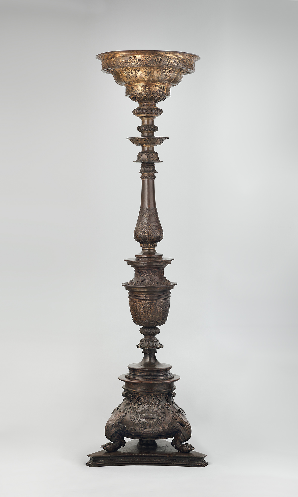 A tall, ornate metal pedestal with intricate carvings and a wide, decorative bowl on top.