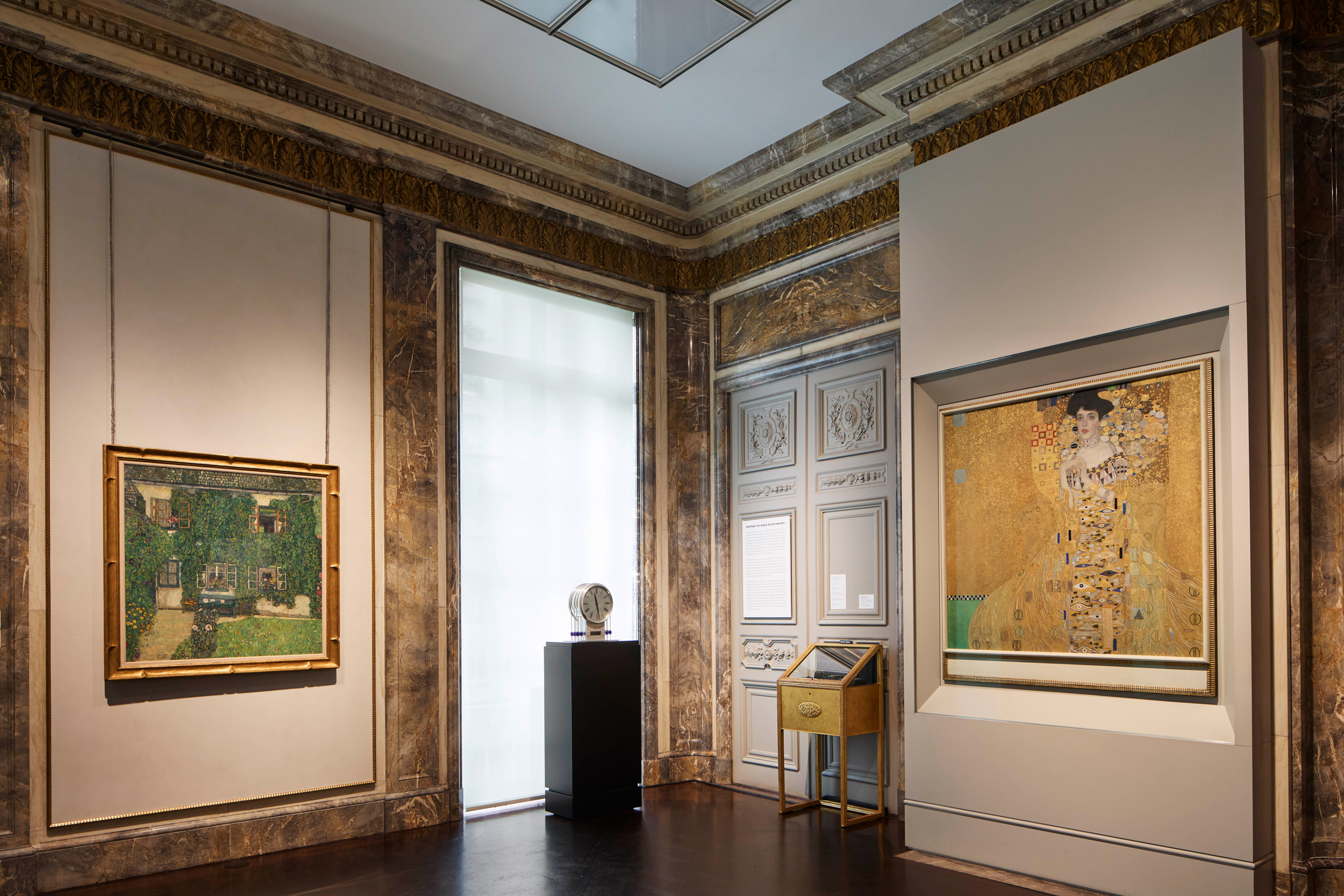 A museum gallery displays two paintings and a sculpture in a room with ornate walls and trim.