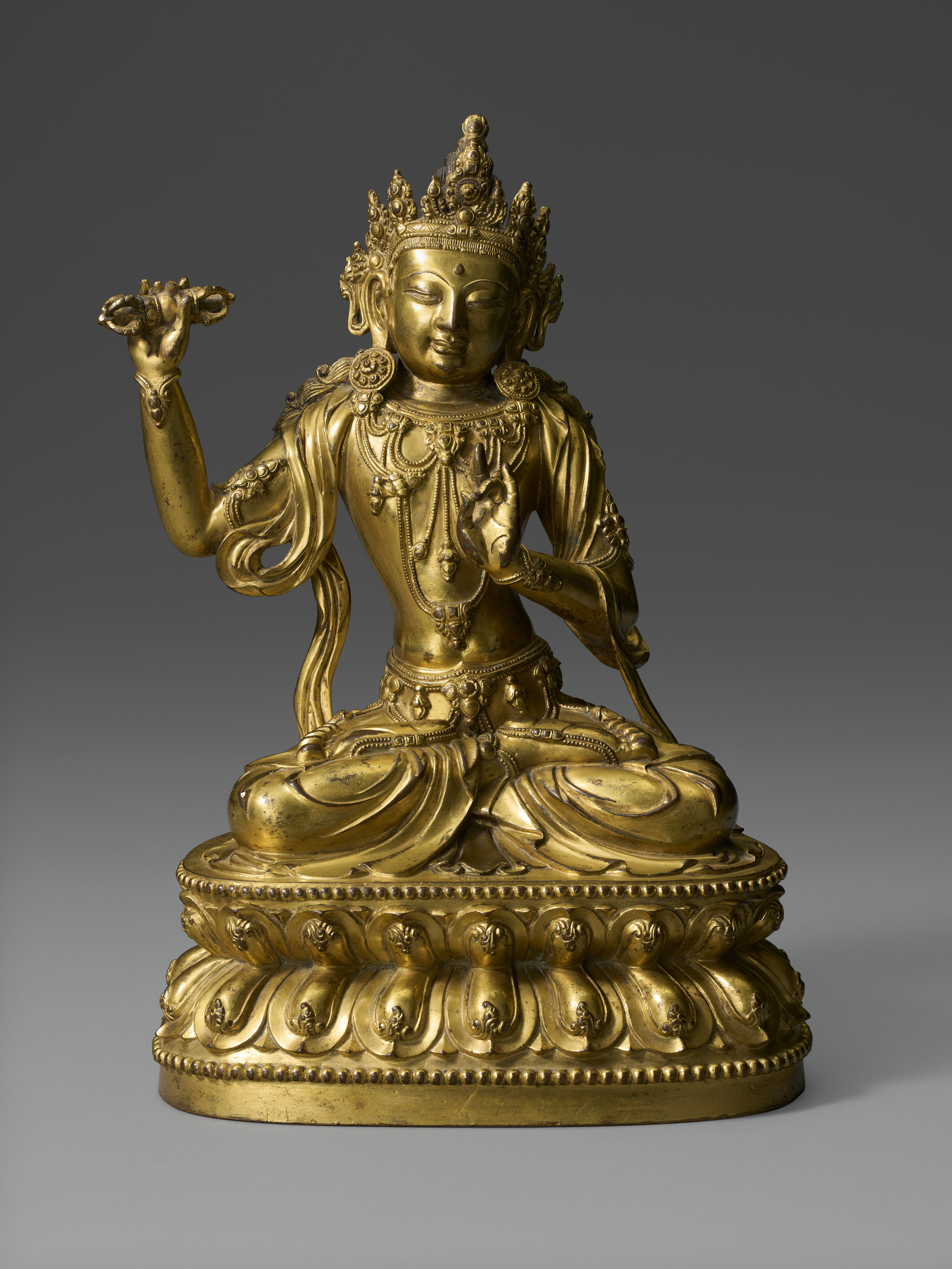 A golden statue of a seated deity with ornate crown and jewelry on a lotus pedestal.
