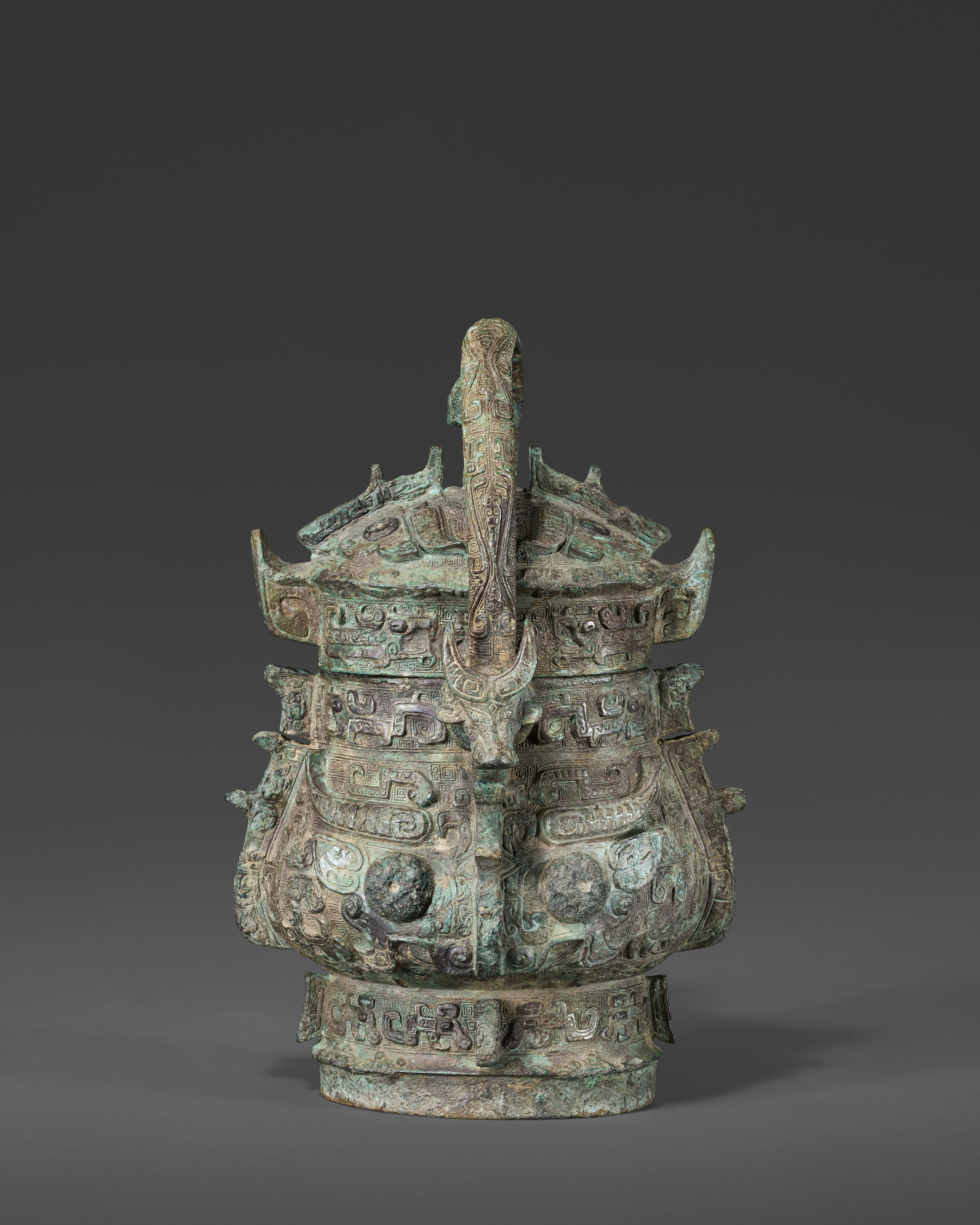 An ancient bronze vessel with intricate carvings and a lid, set against a gray background.