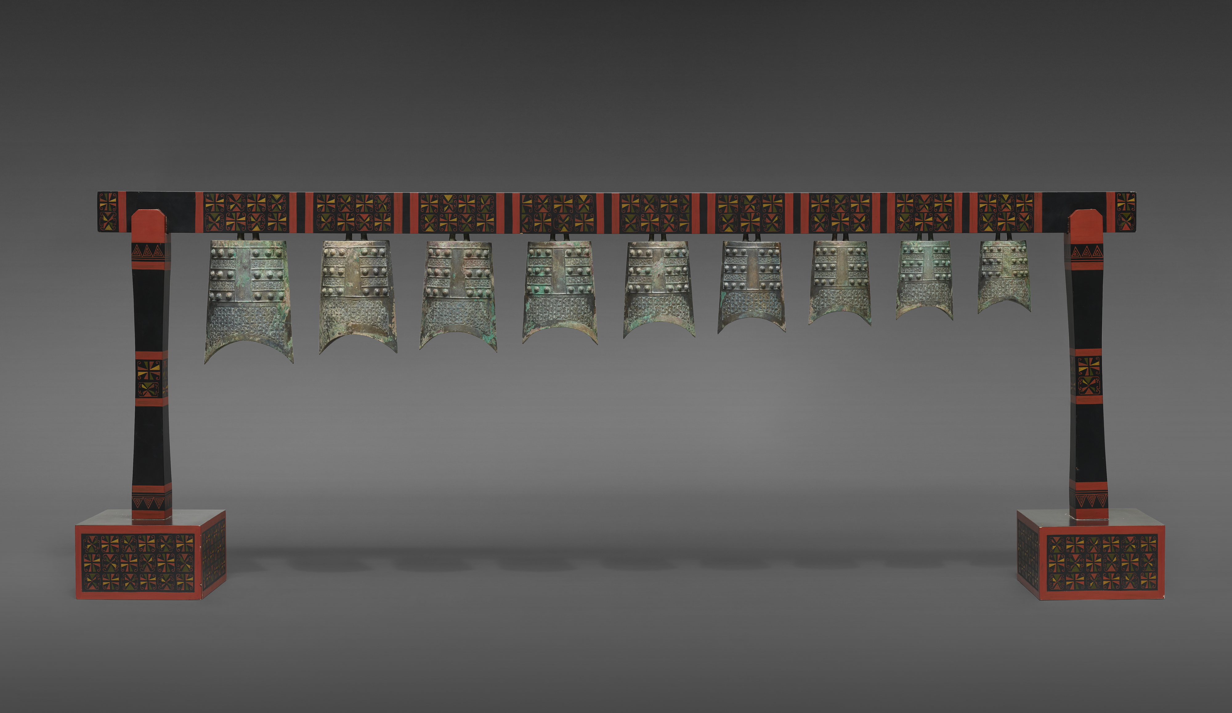 A set of ancient bronze Chinese bells hanging from a decorated wooden frame.