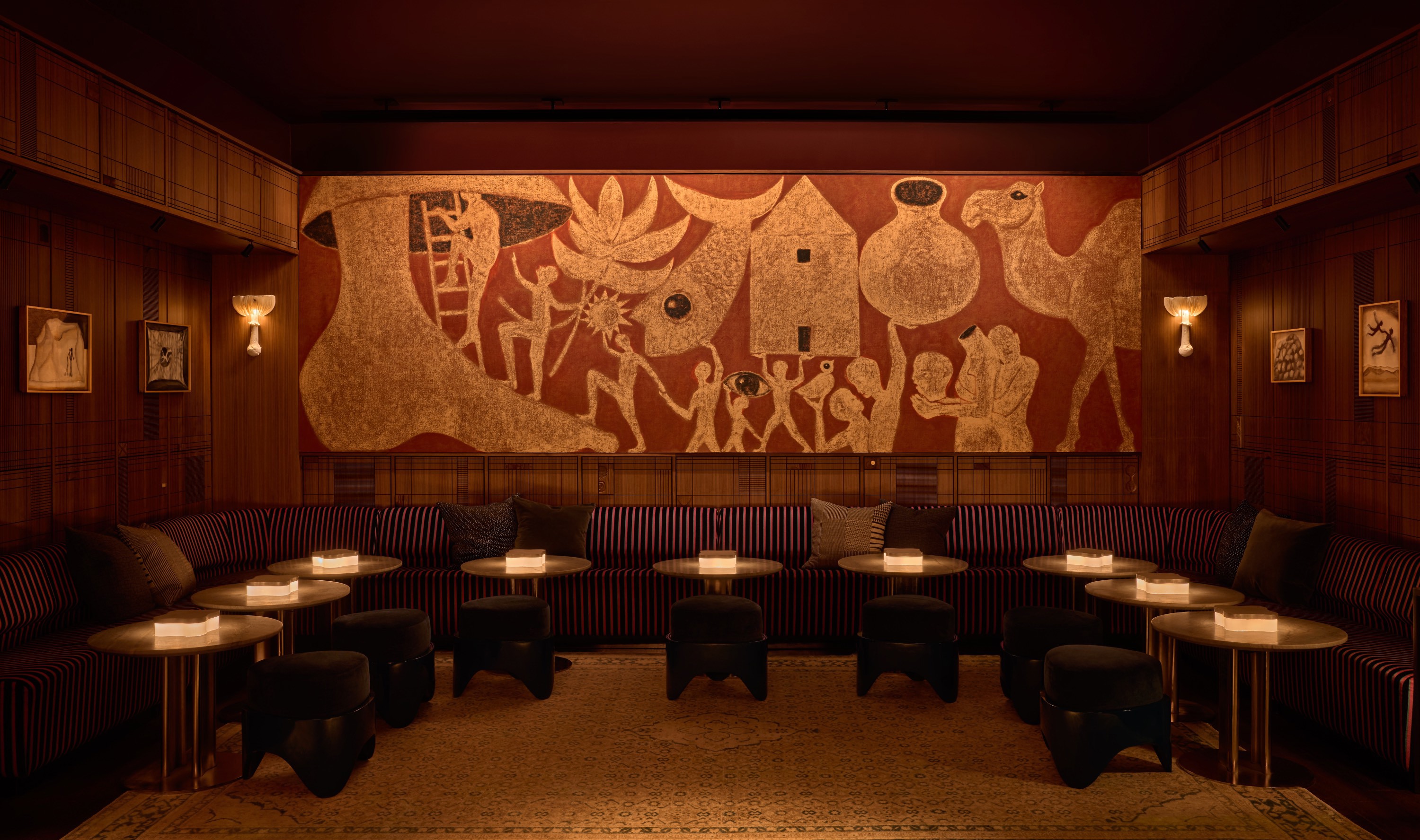 A dimly lit lounge with a large mural, striped seating, and round tables with candles.