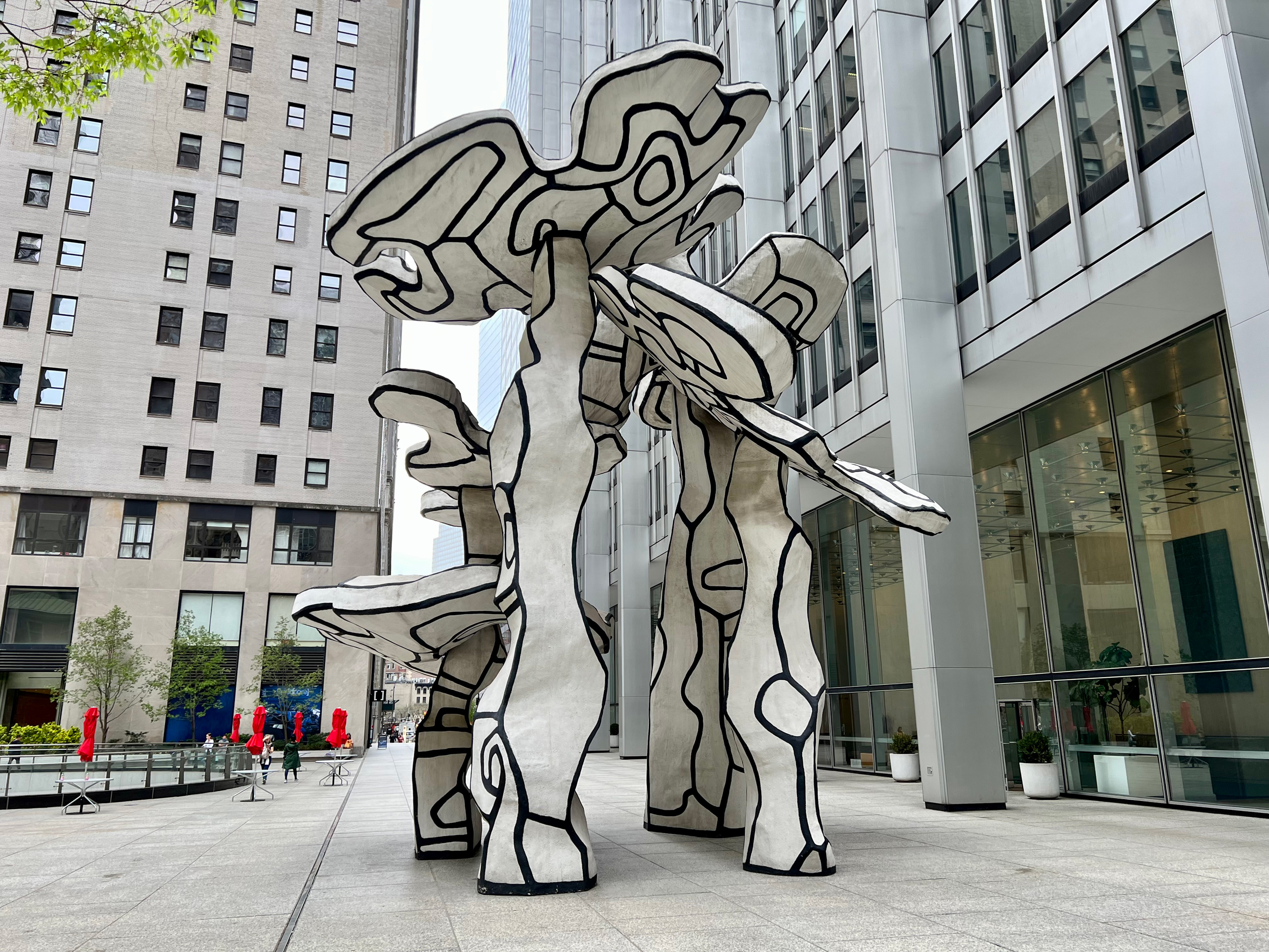 A large abstract black and white sculpture stands in a city plaza surrounded by tall buildings.
