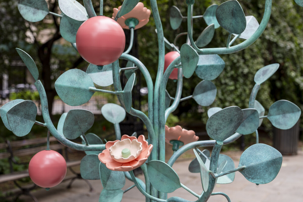A metal sculpture of a plant with teal leaves and pink flowers and fruit.