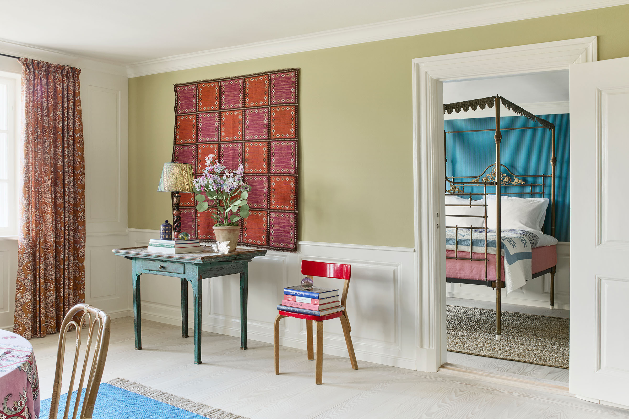 The dining room, looking through to one of two bedrooms, with its French antique brass four-poster bed. The wall tapestry is a rare work by Marta Maas-Fjetterstrom made to a design from 1926 called 'Squares'. The red lacquered chair is by Alvar Aalto; the curtains are by Braquenie