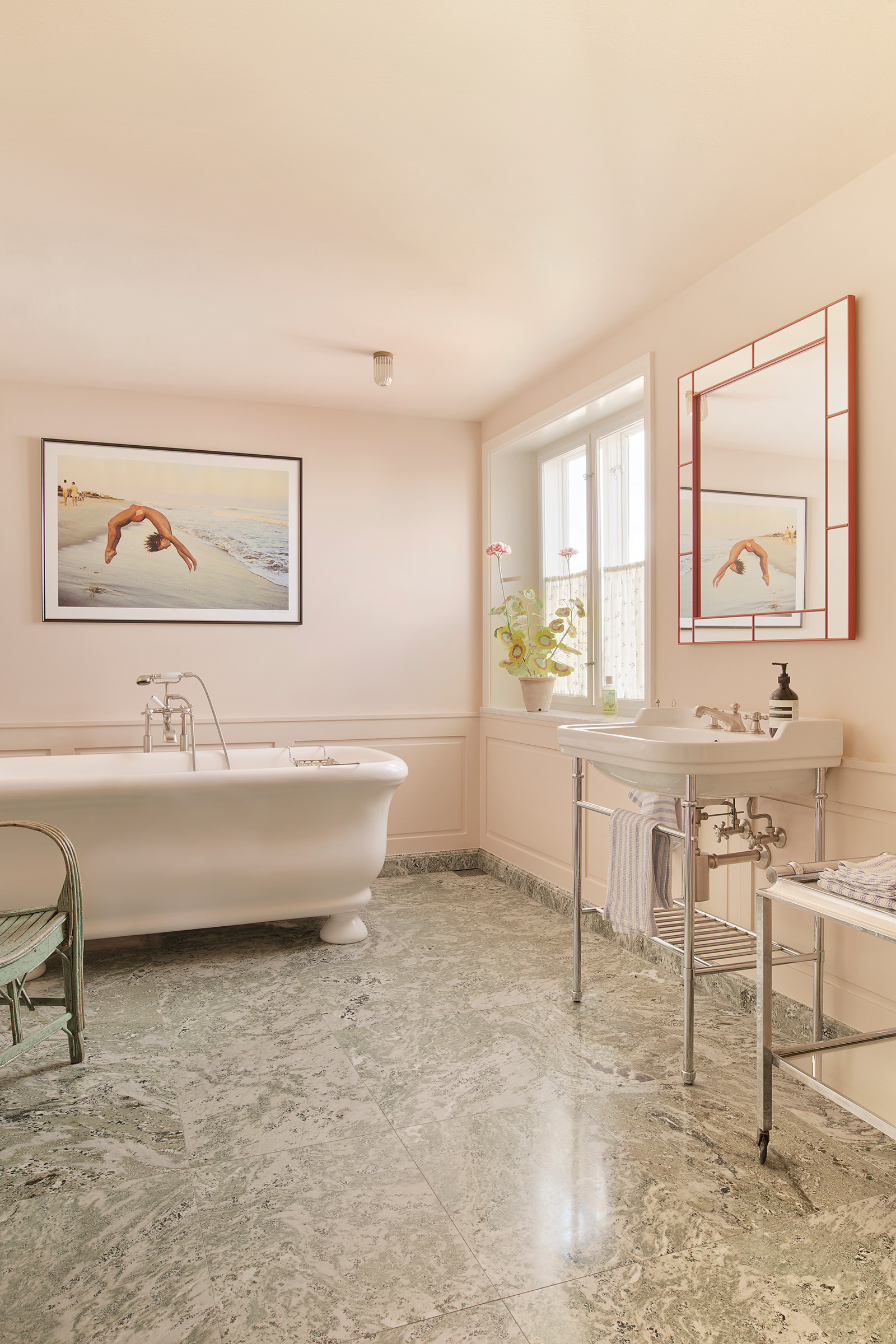 The bathroom has a freestanding bath and green Swedish marble flooring. On the wall is a photograph from 1980 by Peter Schlesinger: Photographer Reto Guntli doing a backflip, Fire Island Pines. The mirror was designed by Josef Frank for Svenskt Tenn