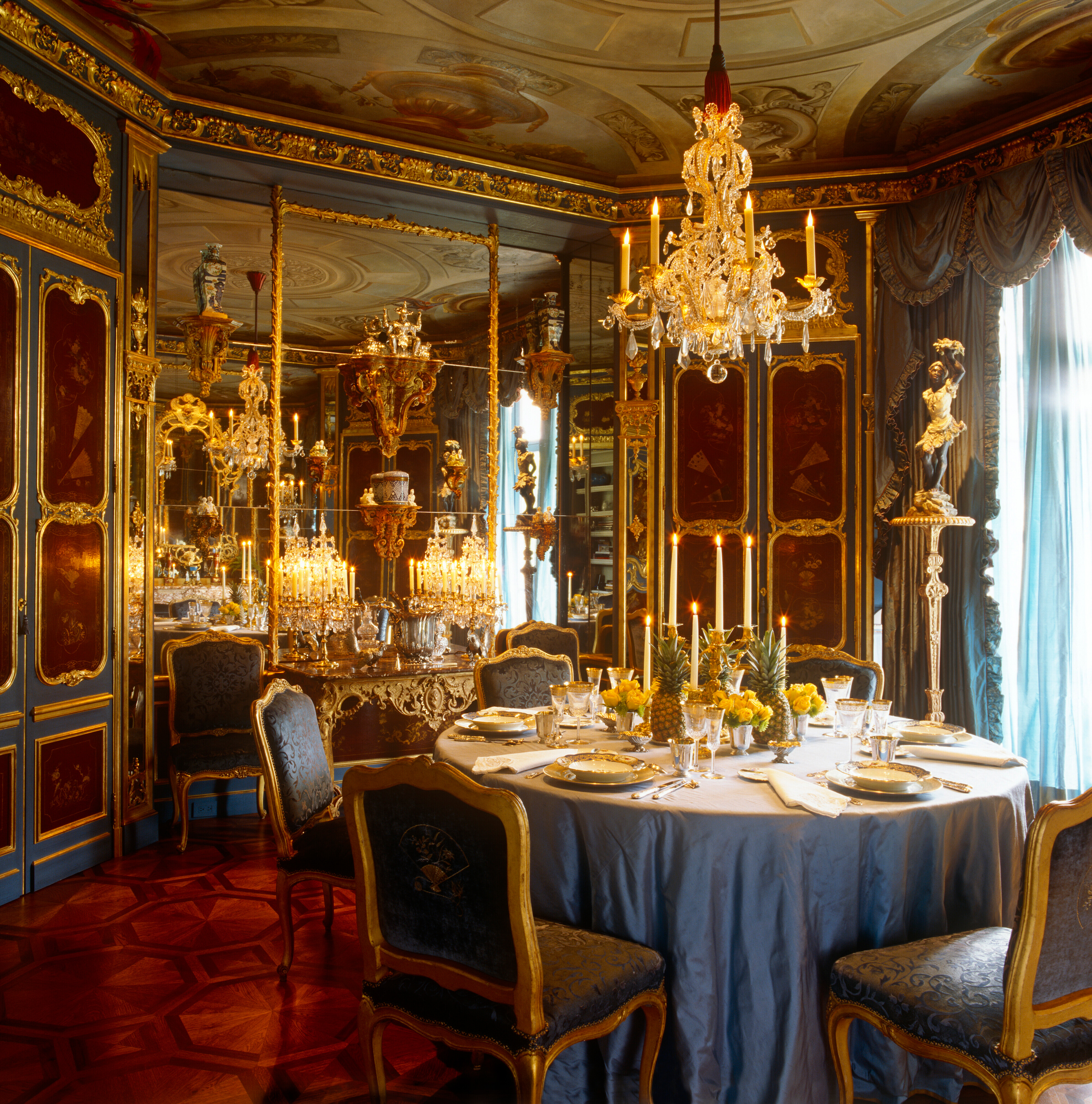 A lavish, ornate dining room features a round table set with elegant dinnerware and golden decor.