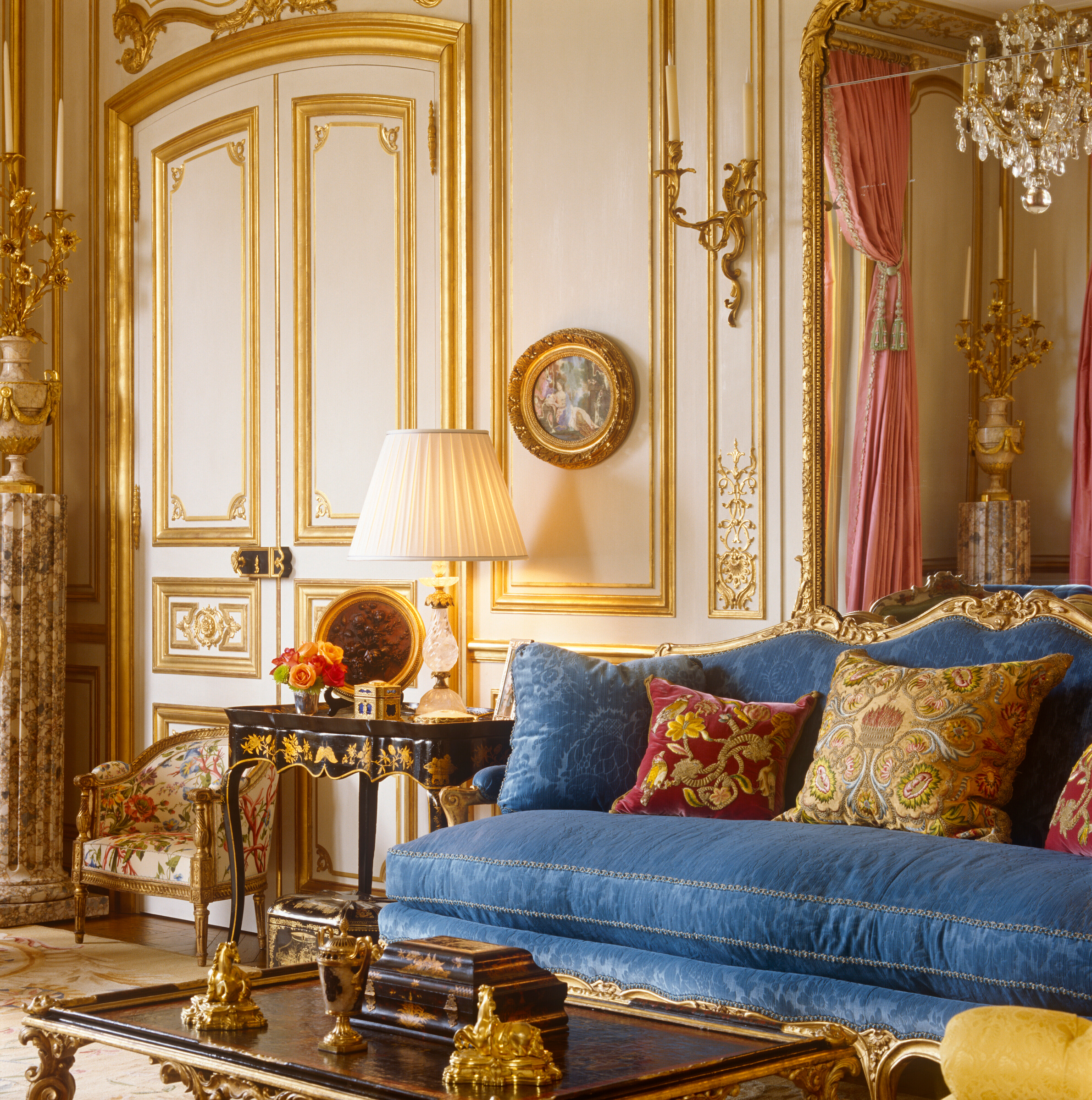 Elegant living room with ornate gold accents, a blue sofa, and luxurious decor items.