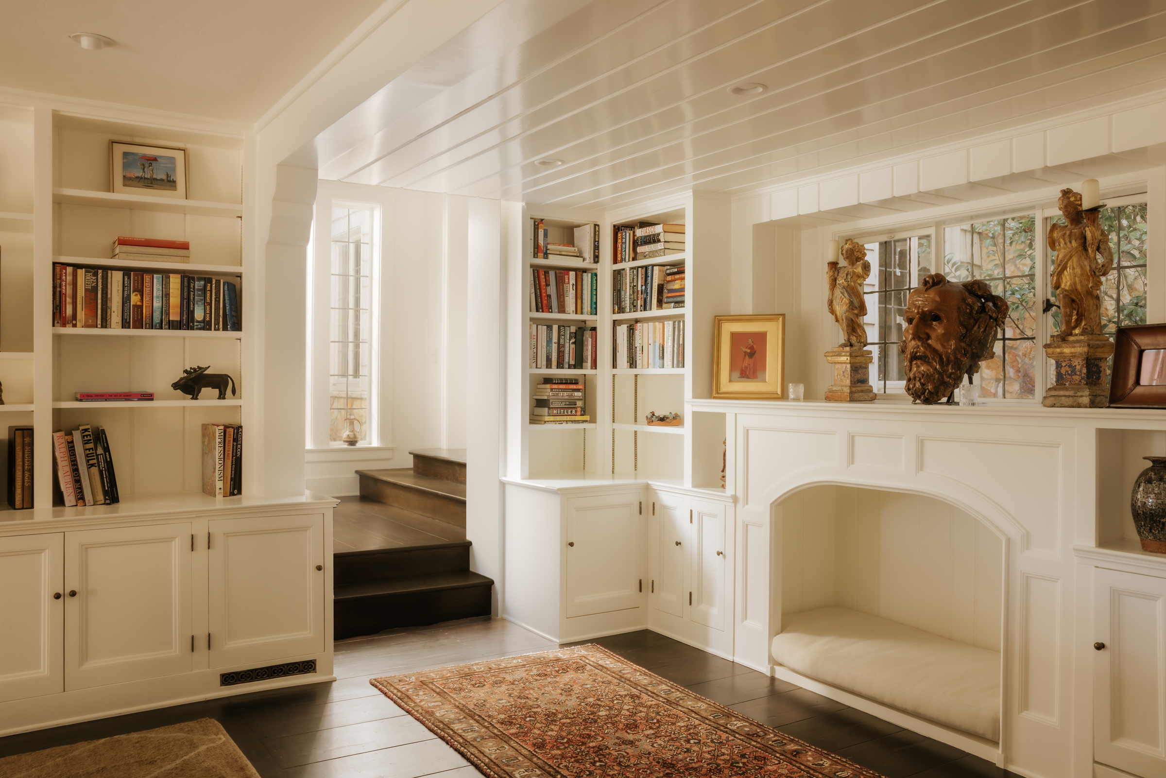 A cozy room features built-in bookshelves, a fireplace, statues, and a patterned rug.