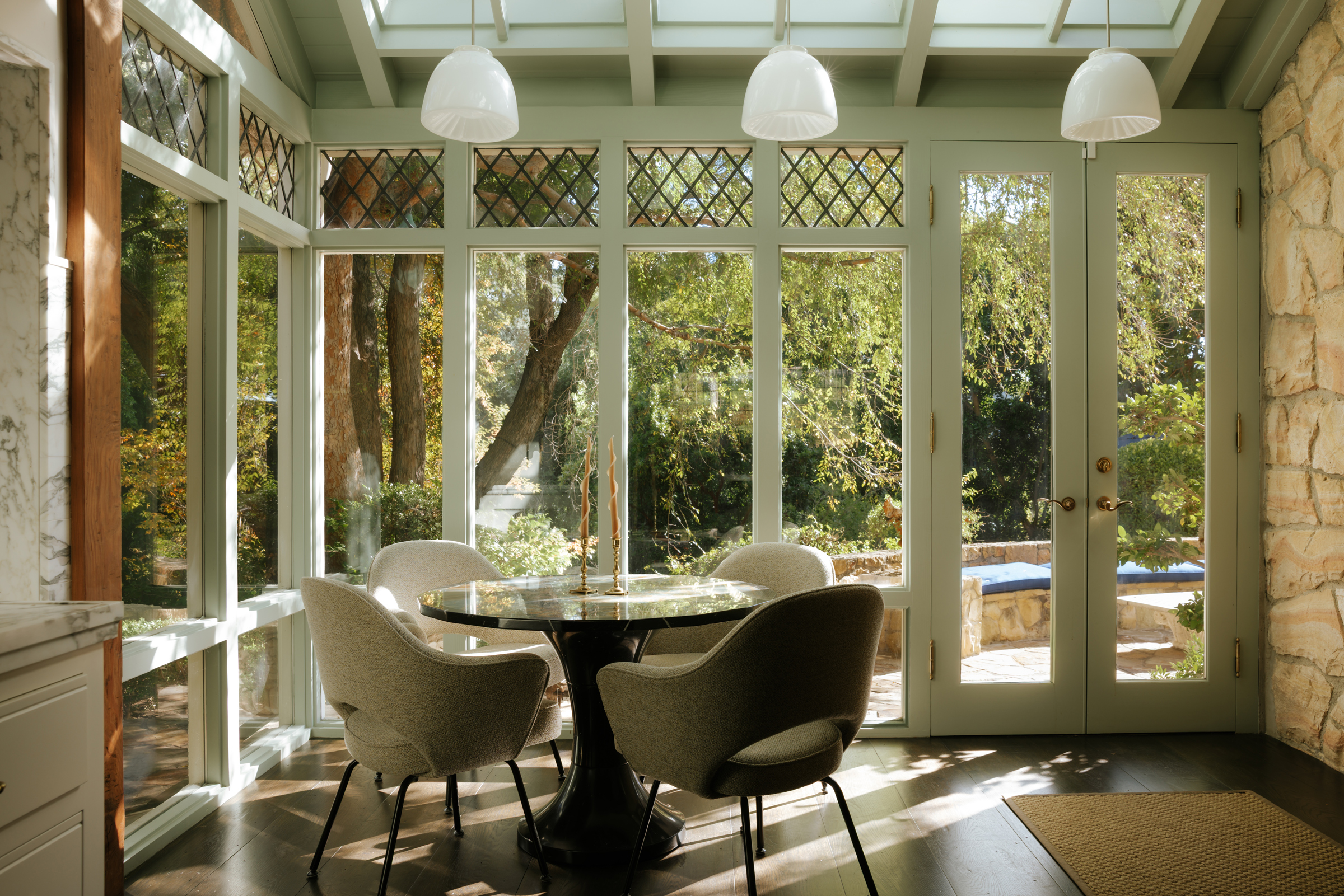 A cozy dining area with four chairs, a round table, and large windows overlooking a garden.