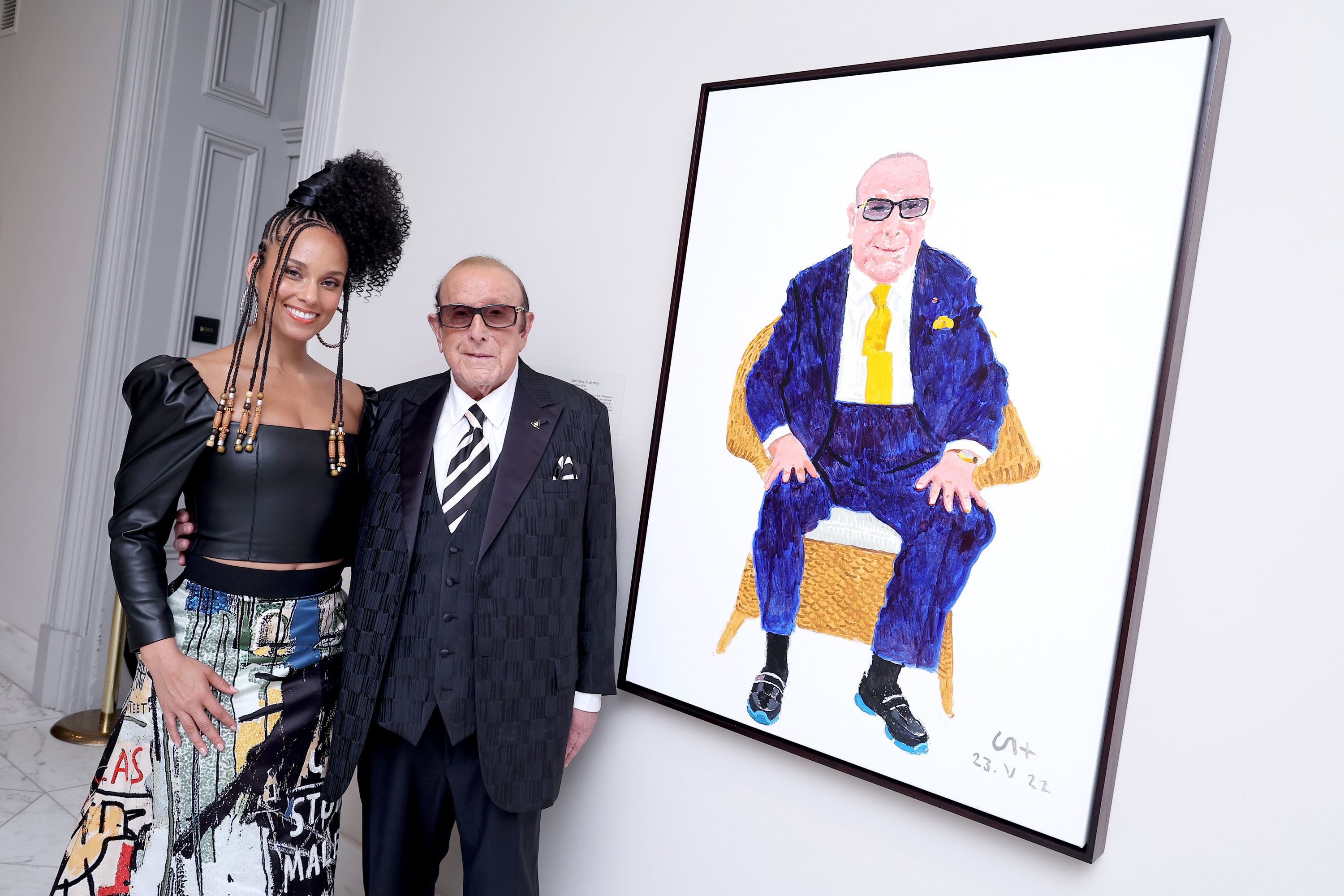 A woman and an older man stand together next to a colorful portrait of the man in a suit.