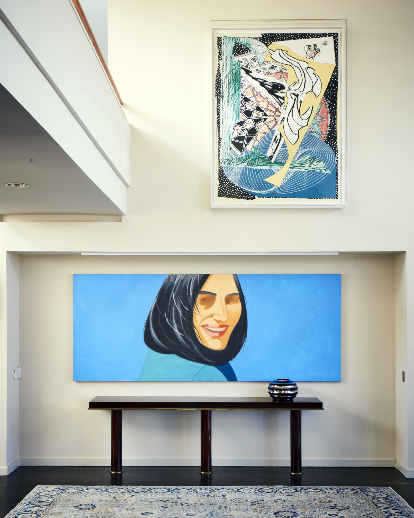 A modern interior with two large colorful artworks, a console table, vase, and a patterned rug.