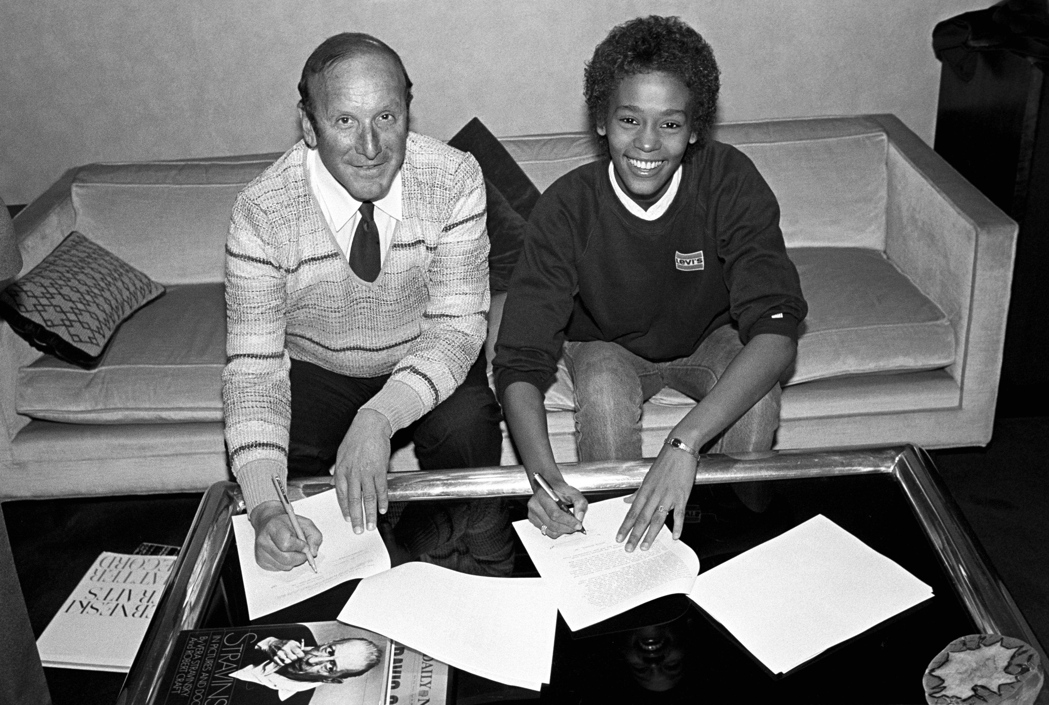 A man and a woman are sitting on a couch, smiling and signing documents on a table.